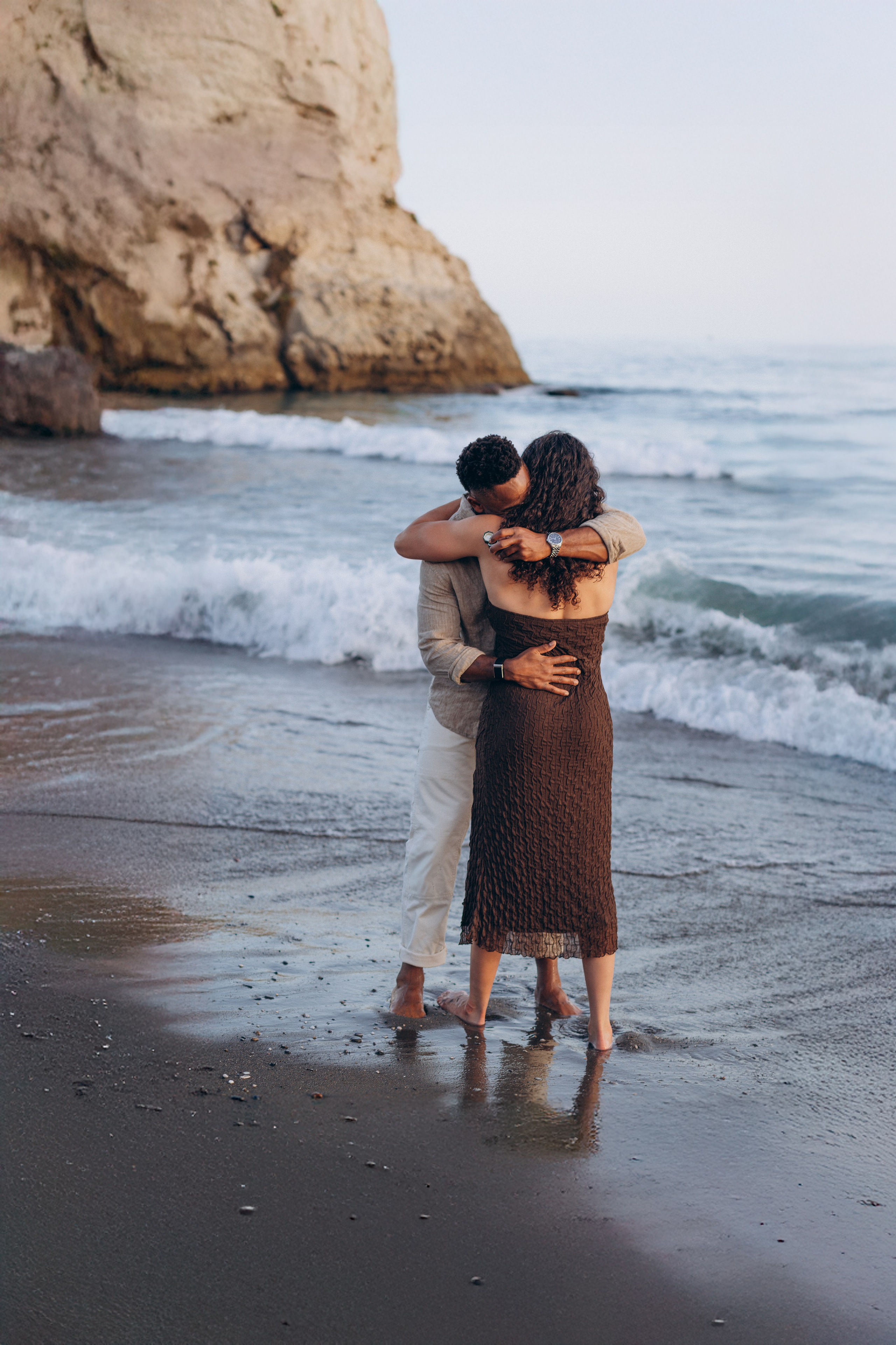 Emotional destination wedding couple session in Málaga, Spain, with bride and groom embracing barefoot by the shoreline during golden hour on the Costa del Sol.