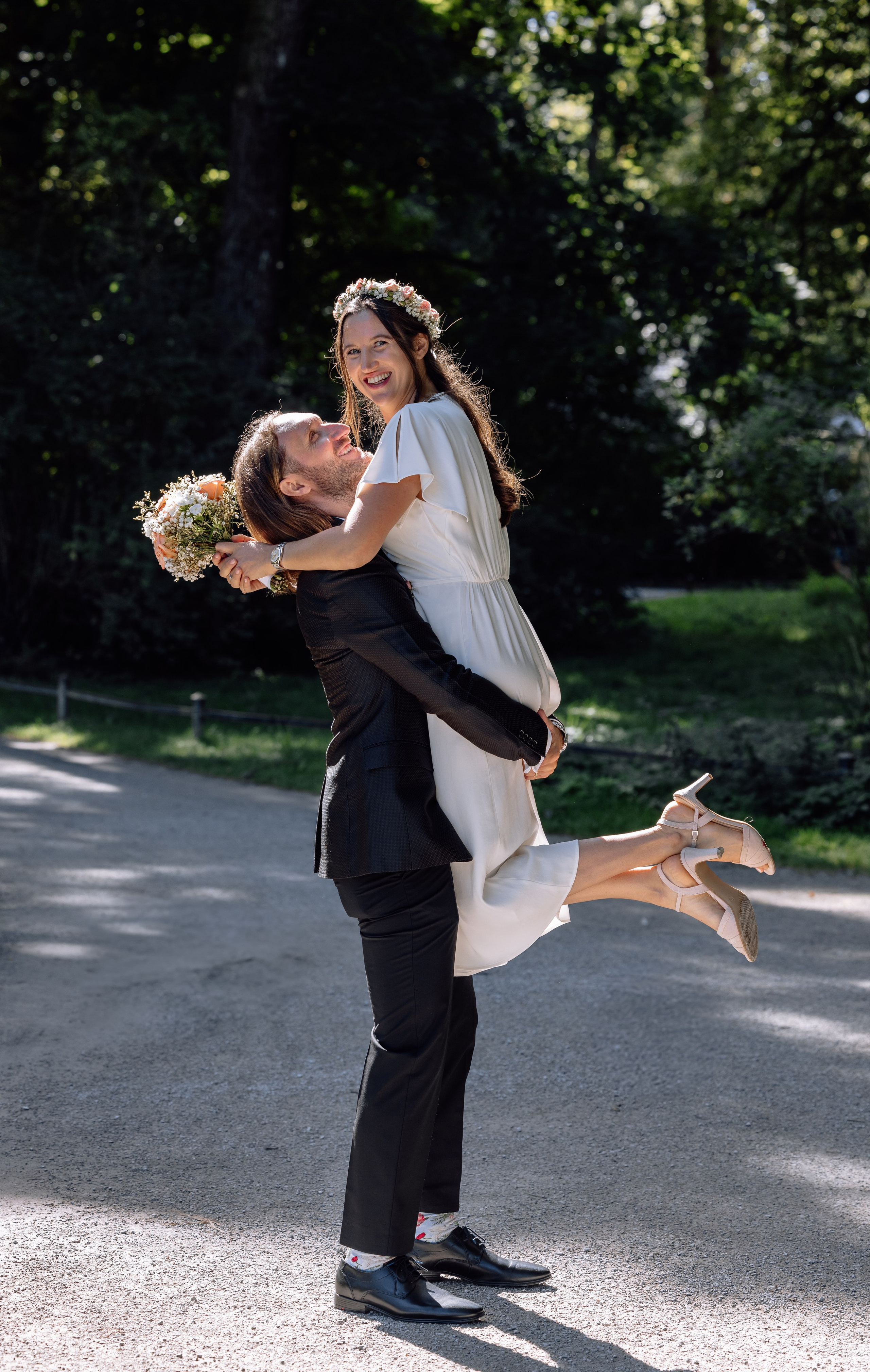 Spaziergang im Englischen Garten – Braut wird vom Bräutigam hochgehoben, natürliche Lichtstimmung