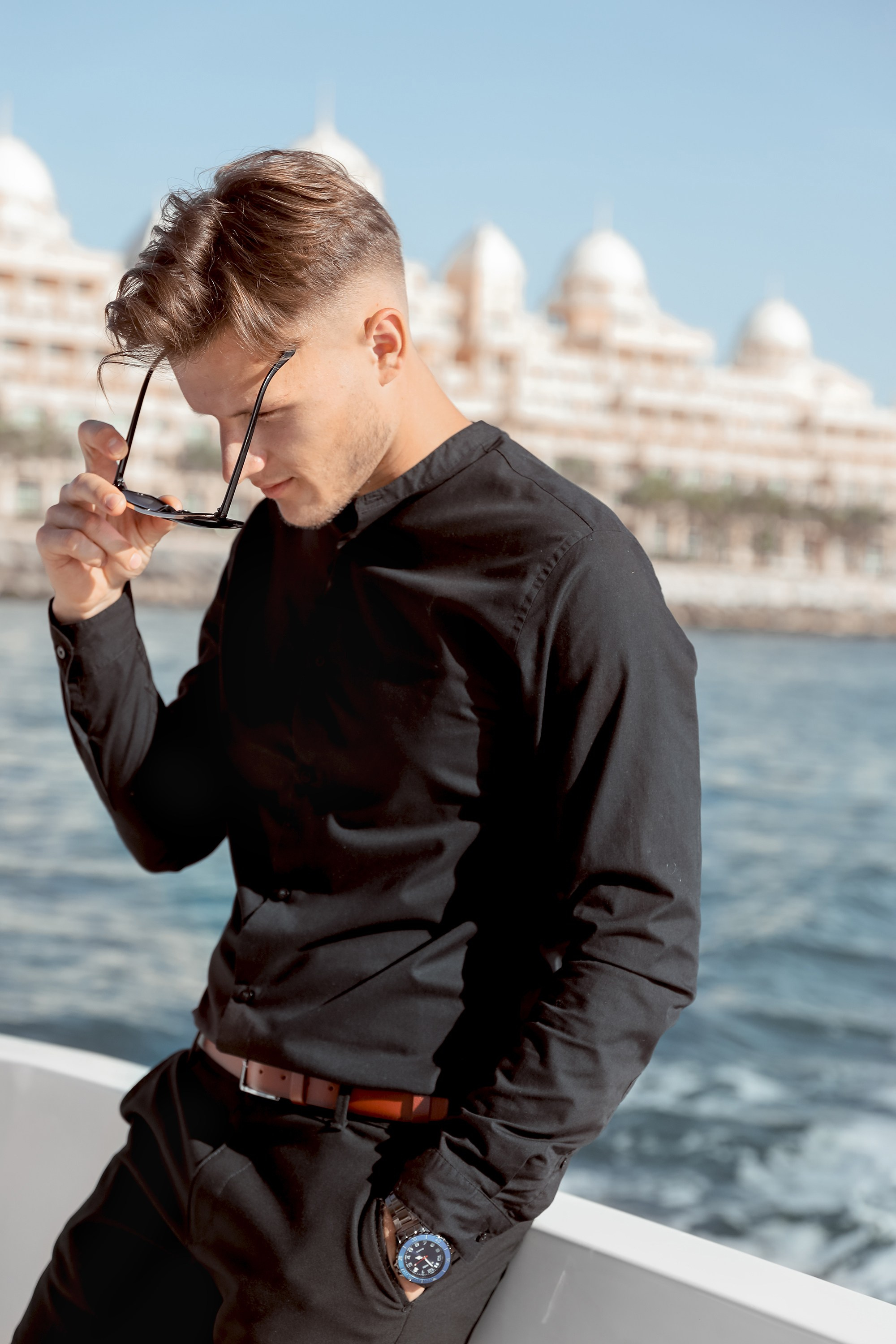 A man stands confidently on a yacht, his gaze warm and relaxed as the ocean breeze flows through his hair, with the sea stretching behind him. Dubai, United Arab Emirates