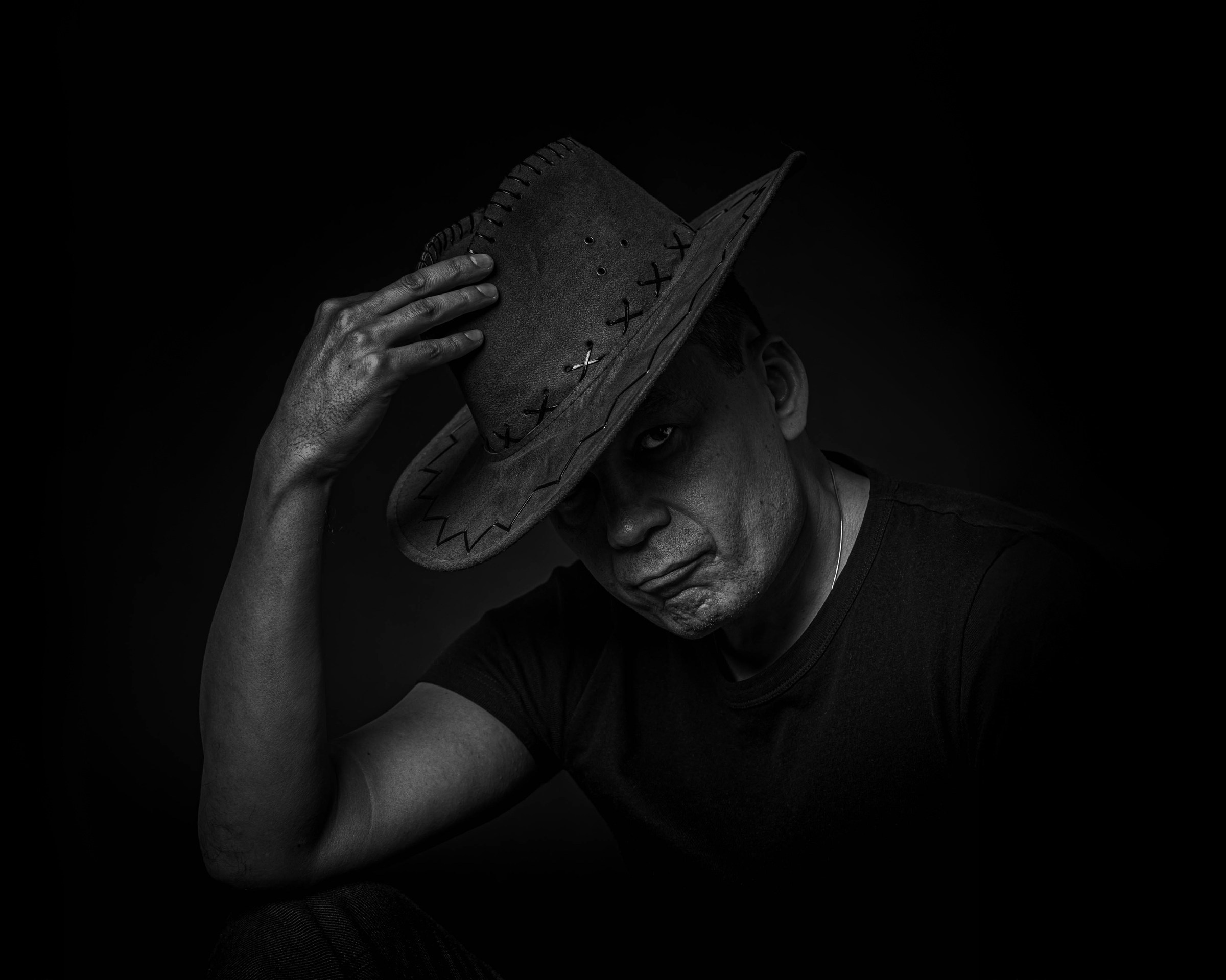 Dark portrait of a man adjusting his hat with his head lowered