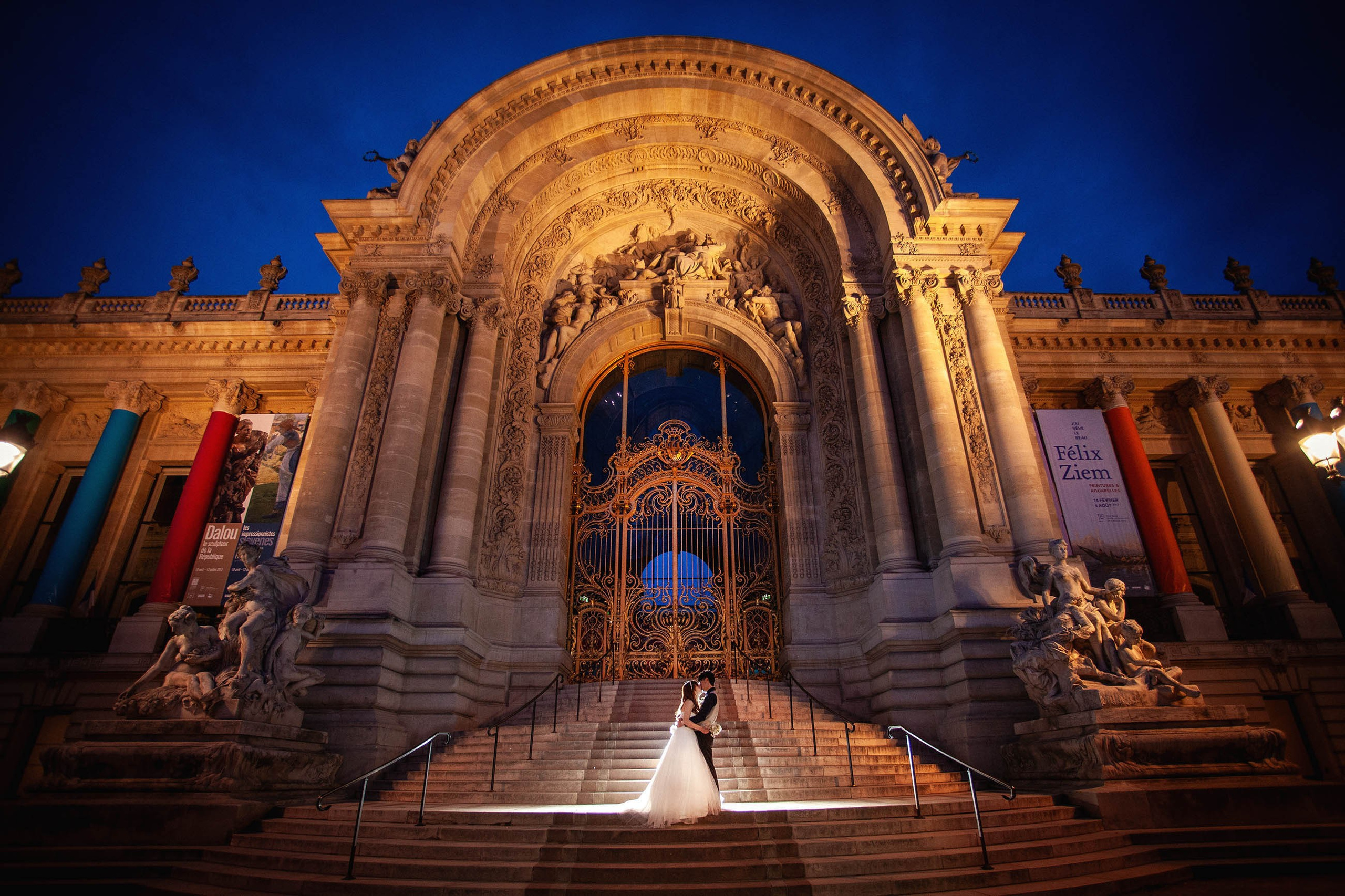 Newlyweds share a romantic kiss on the steps of the iconic Petit Palais in Paris during their nighttime portrait session.