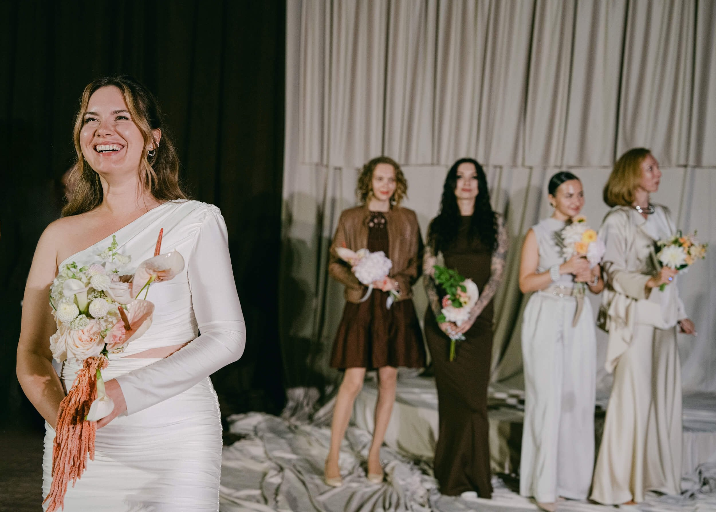 Bride and groom standing together in front of a light grey curtain backdrop with a large floral arrangement, elegant wedding portrait at Lake Como