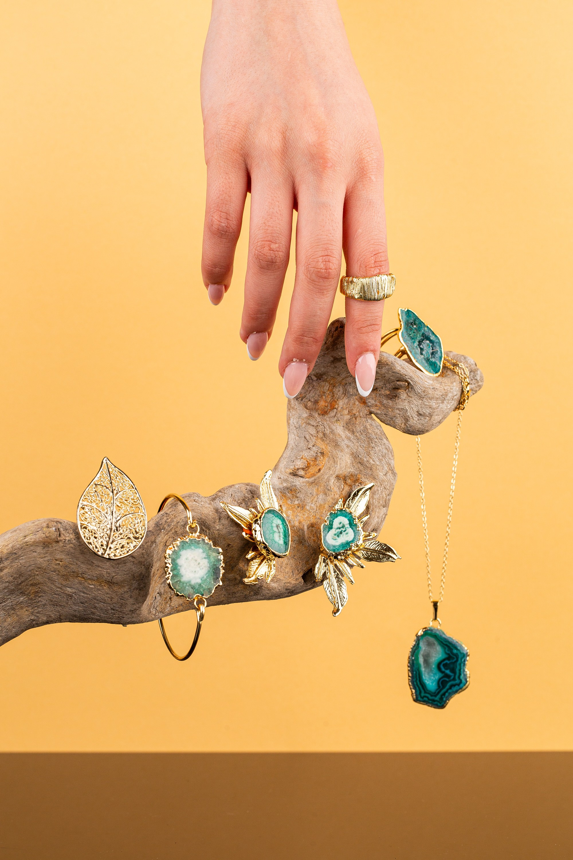 Üzük, bilərzik və boyunbağı olan driftwood parçası üzərində təbii əqiq daşları olan qızıl zərgərlik.