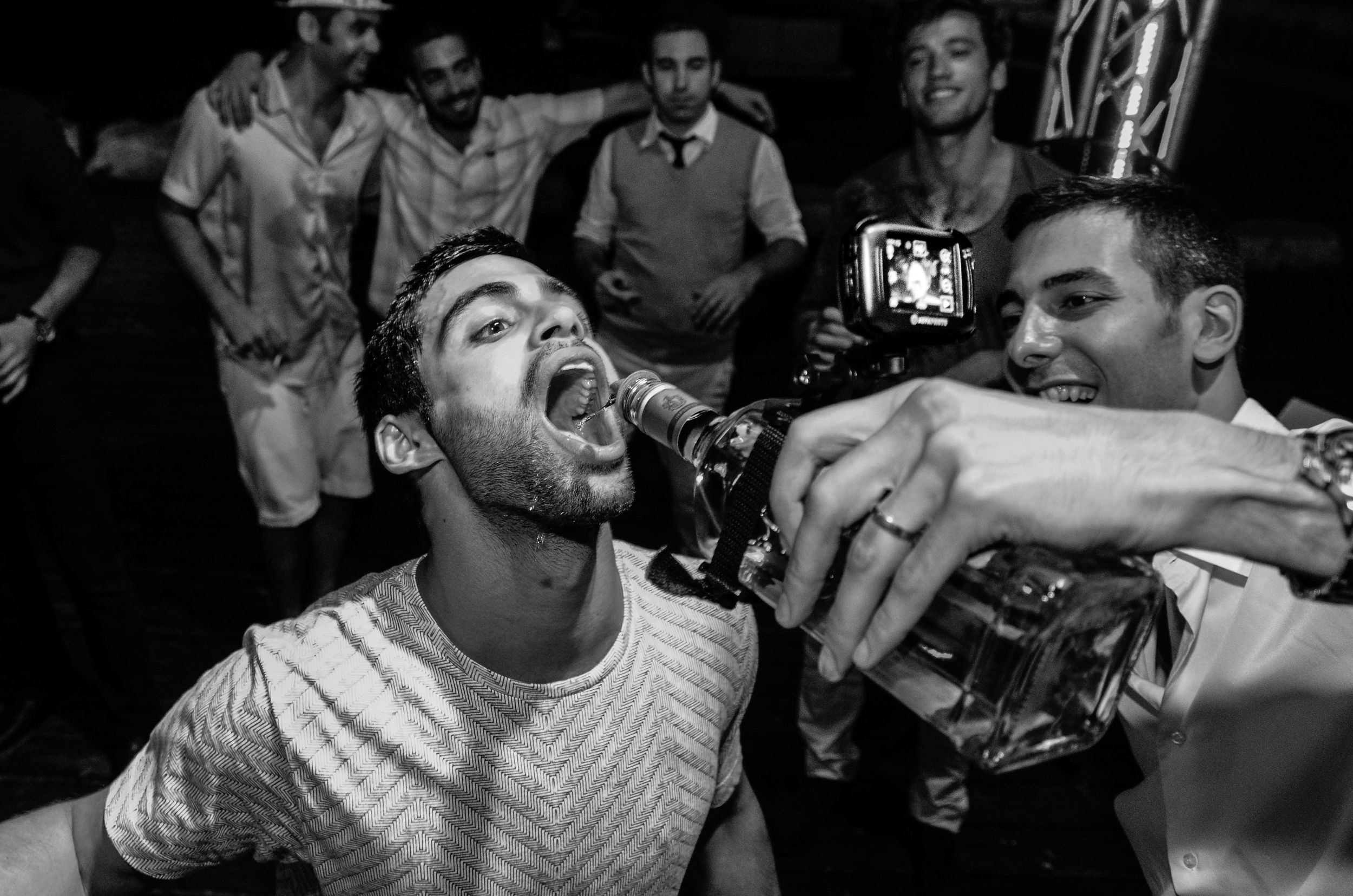 Groom and friends celebrating at a wedding party, pouring a drink straight from the bottle. 