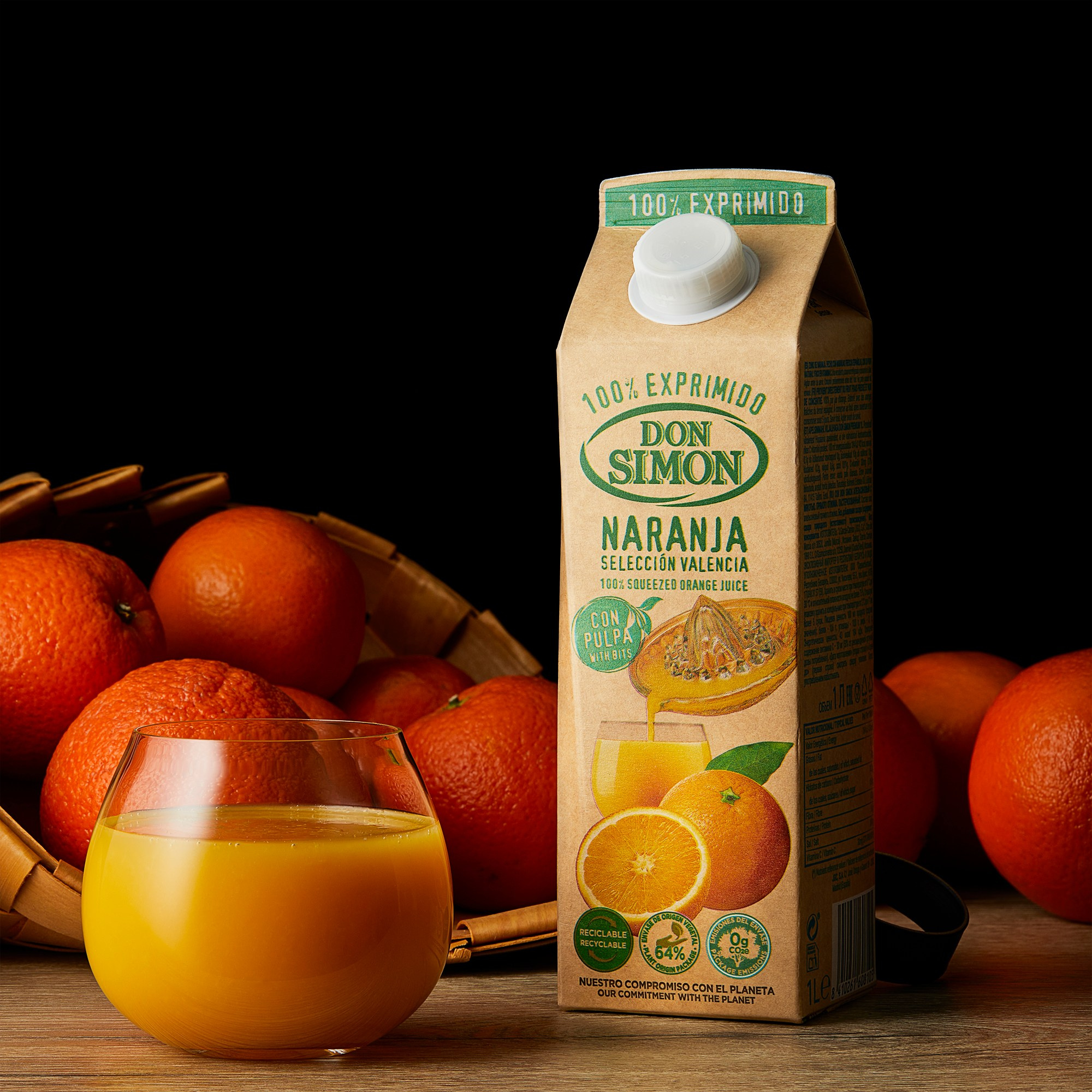 Photographer Roman Djuzev - The photograph shows Don Simon brand orange juice poured into a transparent glass, with a juice carton placed next to it. Behind the glass and the carton, part of a basket with oranges is visible, and the background is dark.