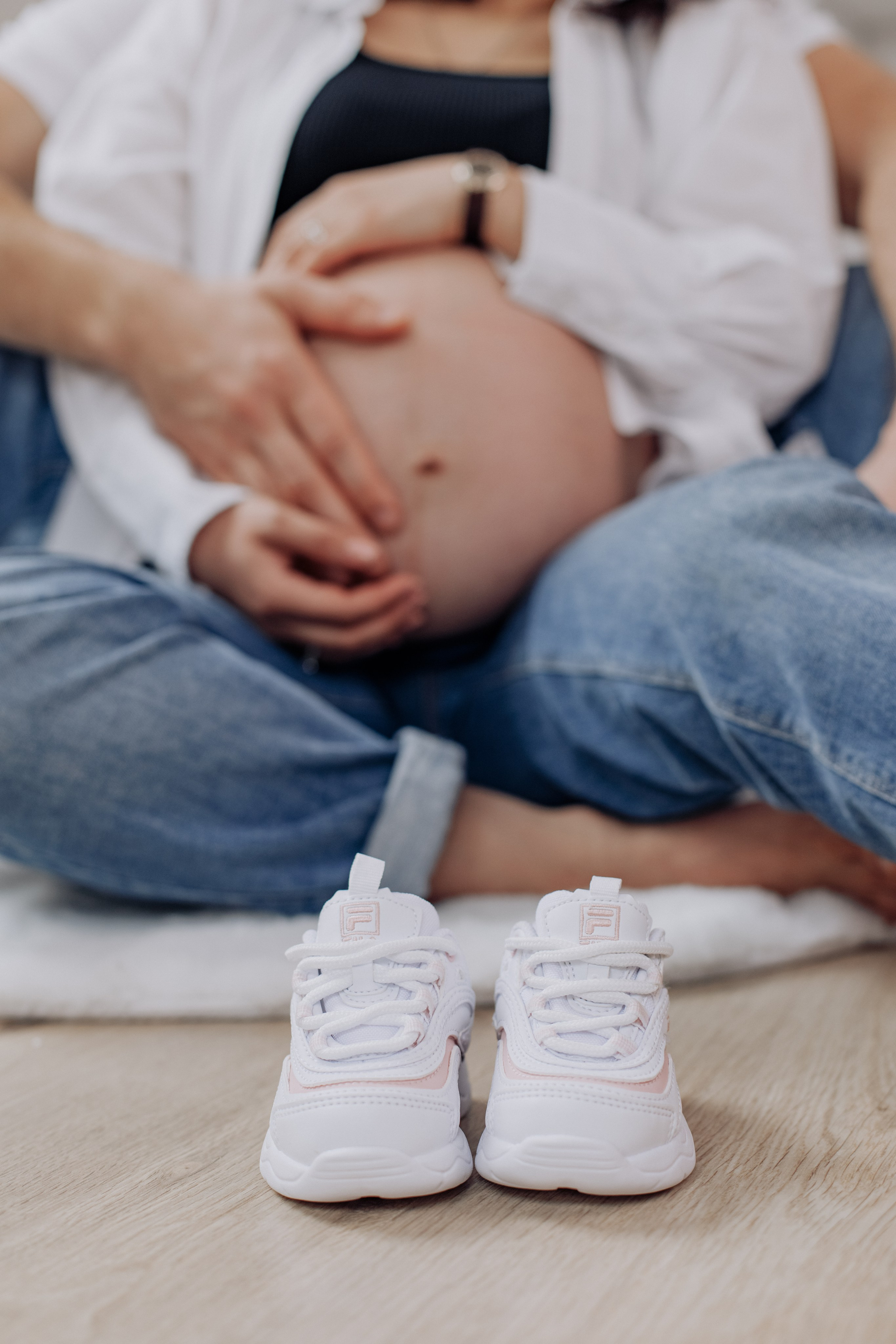 Stylische Babyschuhe stehen im Vordergrund vor dem Babybauch einer schwangeren Frau im Fotostudio.