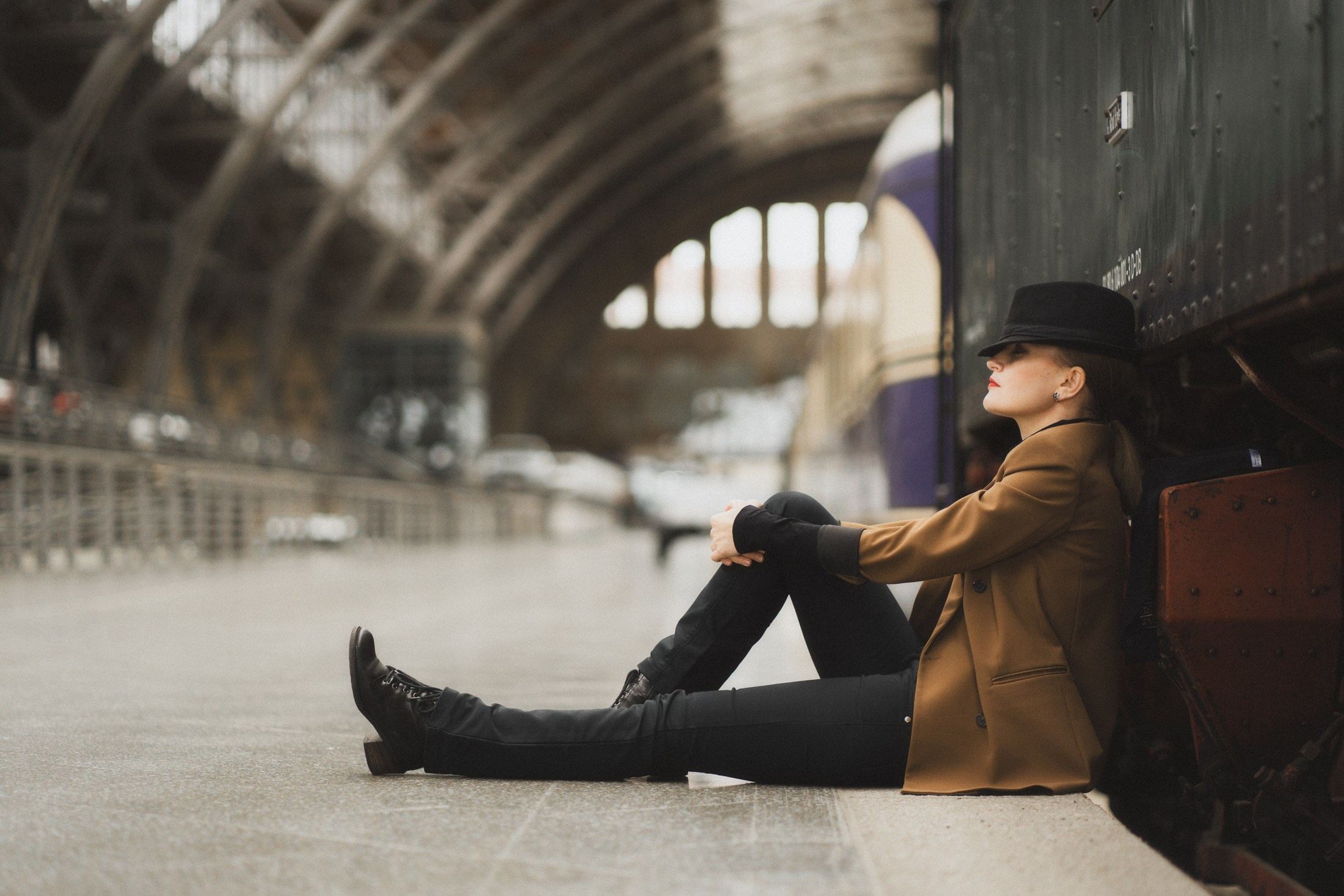 Portrait einer Frau in Mantel und Hut, sitzend auf dem Boden des Bahnhofs – künstlerisches Foto Dresden