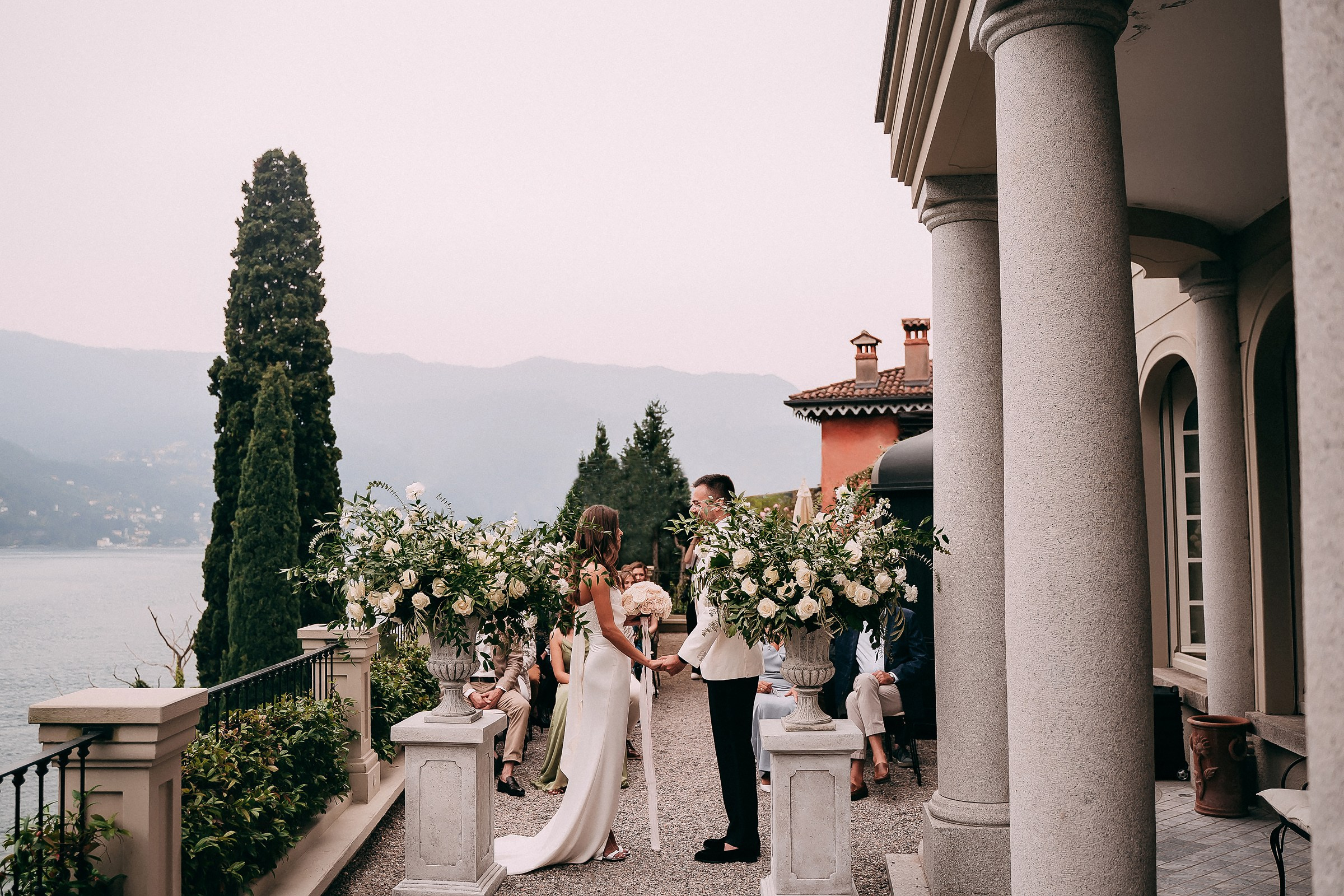 Bride and groom exchanging vows on a romantic villa terrace overlooking Lake Como, surrounded by lush floral arrangements and elegant Mediterranean architecture.
