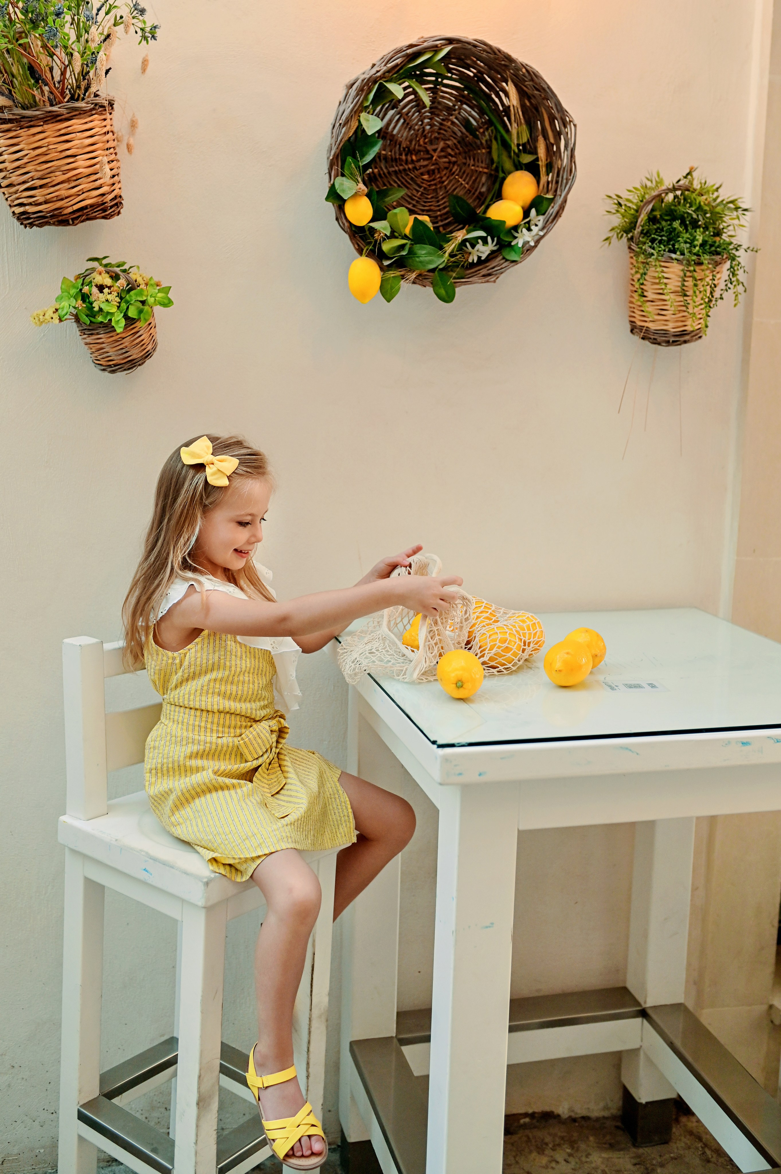 Little girl playing with lemons at a traditional Apulian table decorated with citrus wreath and potted plants, Gallipoli