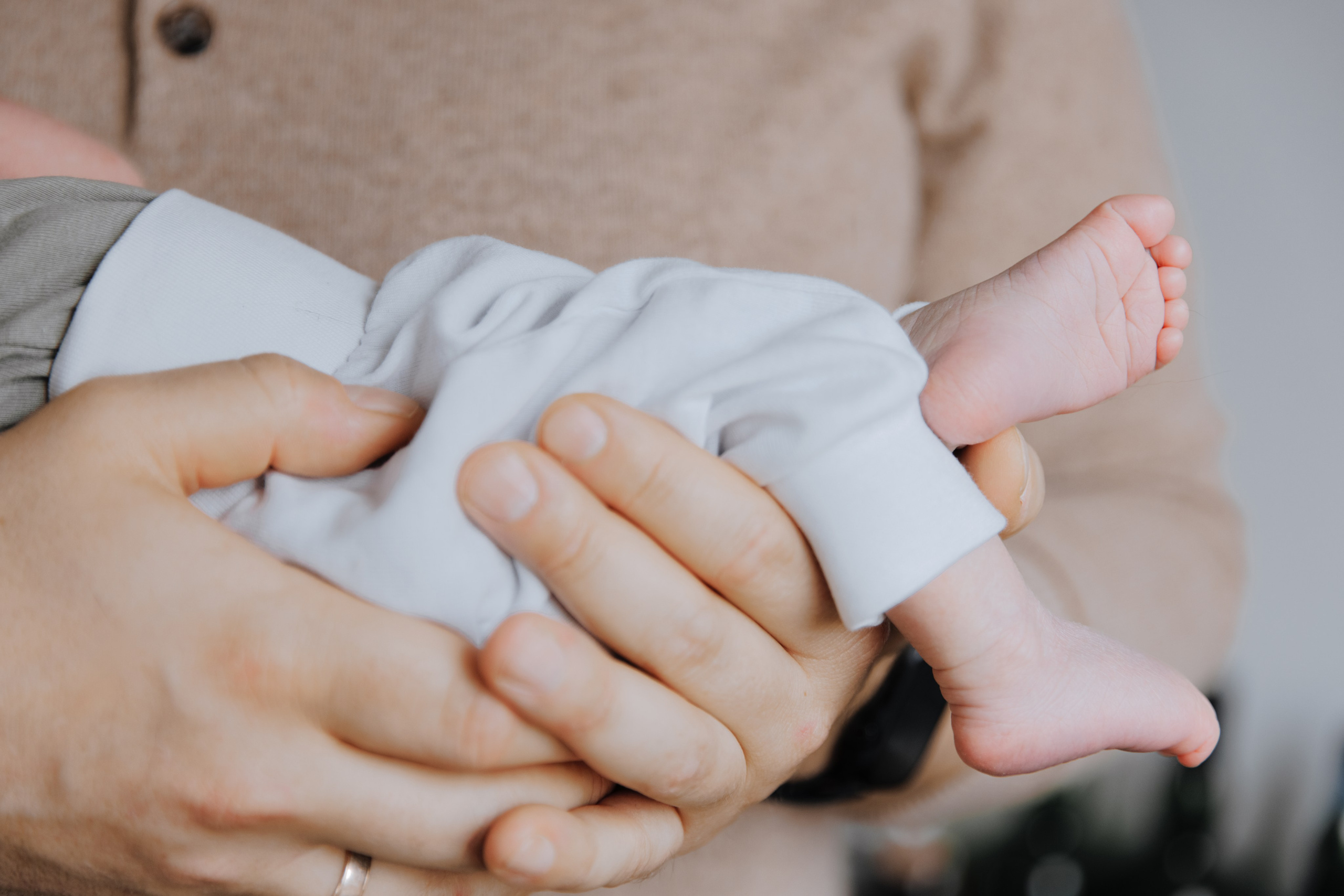 Die kleinen Babyfüße hängen herab, während das Baby in den Armen des Vaters liegt.