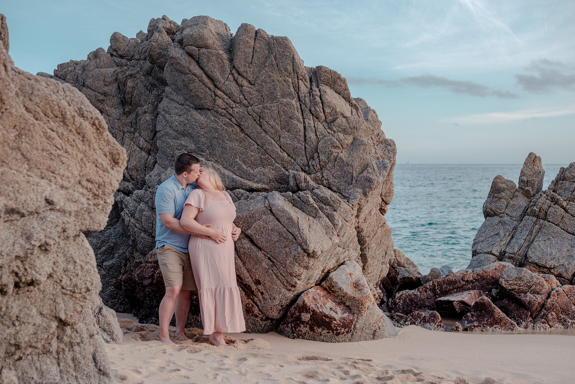 Family of four posing near the rocky coastline of Playa Monumentos with El Arco in the distance Cabo San Lucas