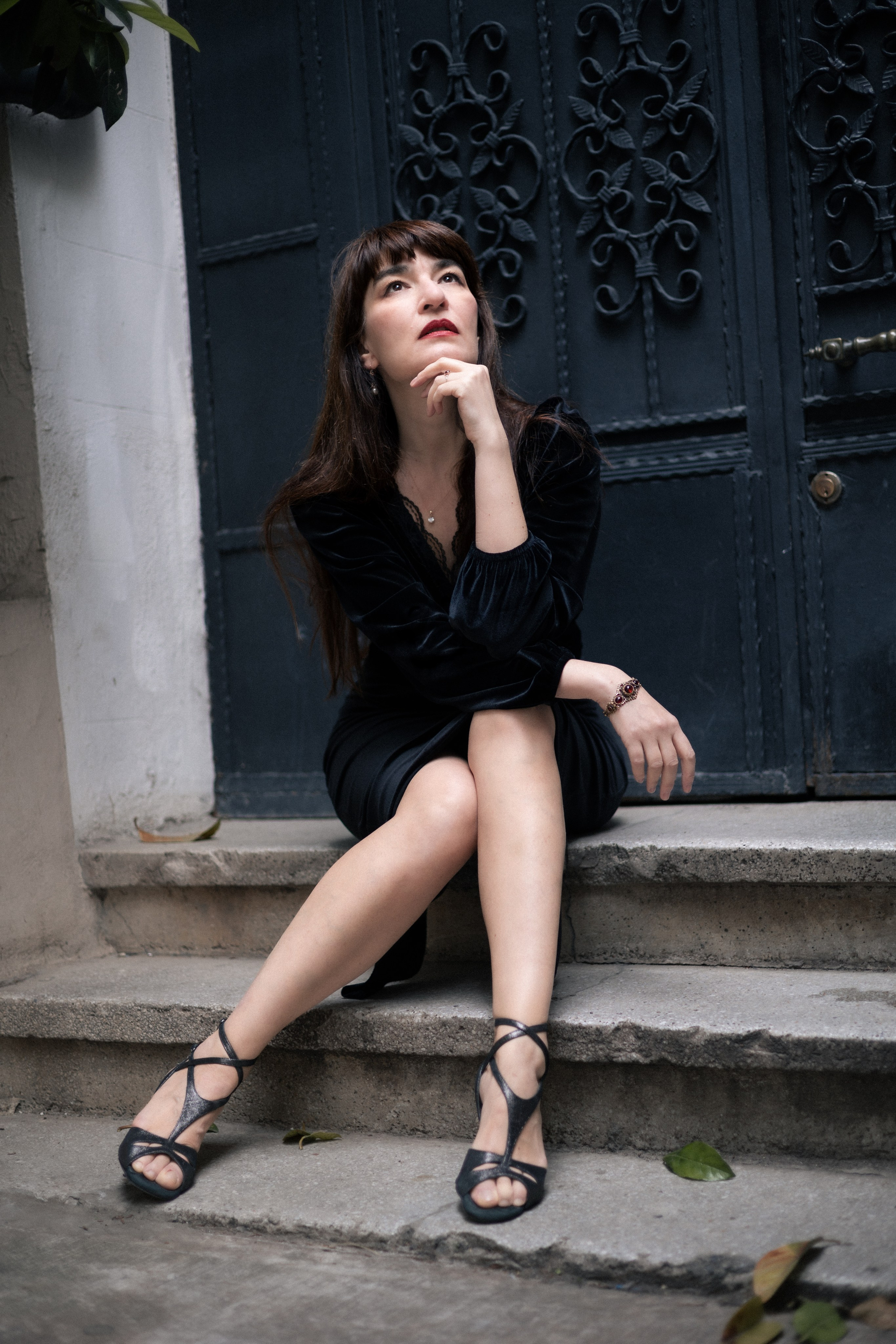 Женщина в чёрном платье сидит на ступенях у декоративной двери и задумчиво смотрит вверх, портрет в городской среде Стамбула