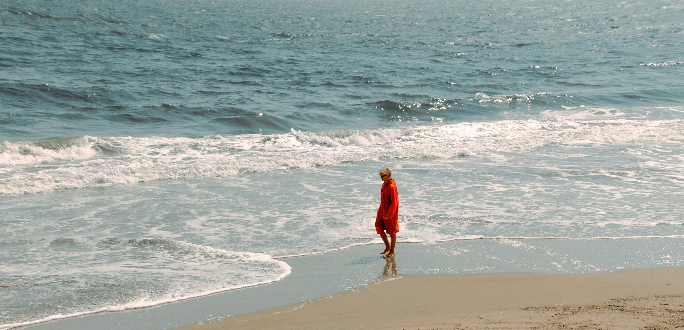 “The last lifeguard”, is a photographic series exploring a solitary figure walking the coastline during low tide. The beach is nearly empty, the water has withdrawn, and the lifeguard — dressed in a red coat — becomes a small yet powerful symbol of human presence within a vast natural space.I am drawn to the tension between responsibility and isolation. A lifeguard is someone whose purpose is to protect others, even when there is no one left on the shore. Walking along an empty beach, the figure becomes a quiet witness, a guardian without an audience.By photographing from above and from a distance, I reduce the human form to a moving mark between sand and sea. The coastline becomes a stage for silence, memory, and observation. These images are not tied to a specific location; they reflect an emotional state — the moment when the world feels both beautiful and emptied, and one person carries the meaning of being there. Denis Bold / Photographer (New York/USA)