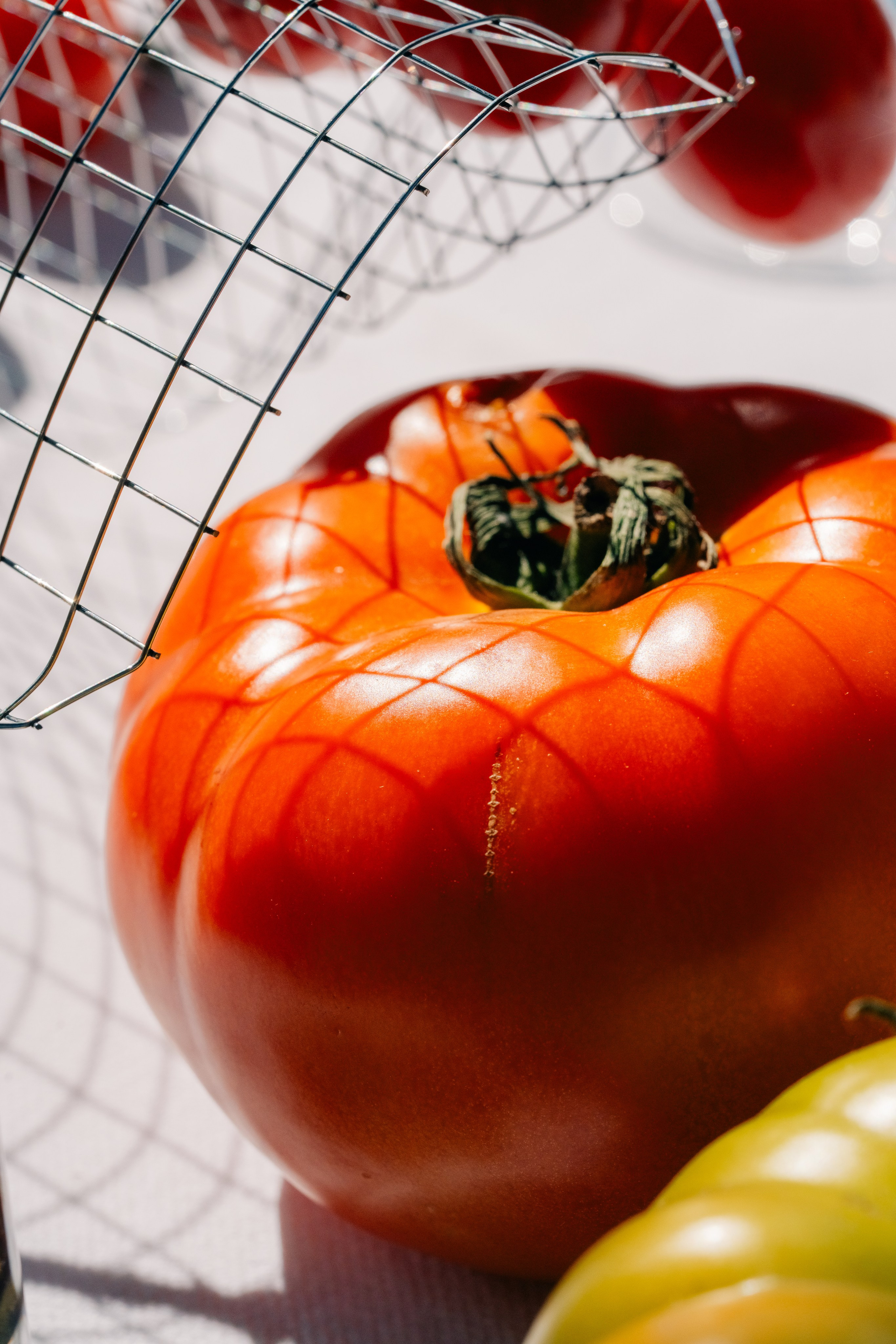 Крупный план освещенного солнцем помидора с узорами из проволочных теней. Детальный крупный план спелого помидора со сложными узорами из проволочных теней на его поверхности, снятый при естественном солнечном свете.