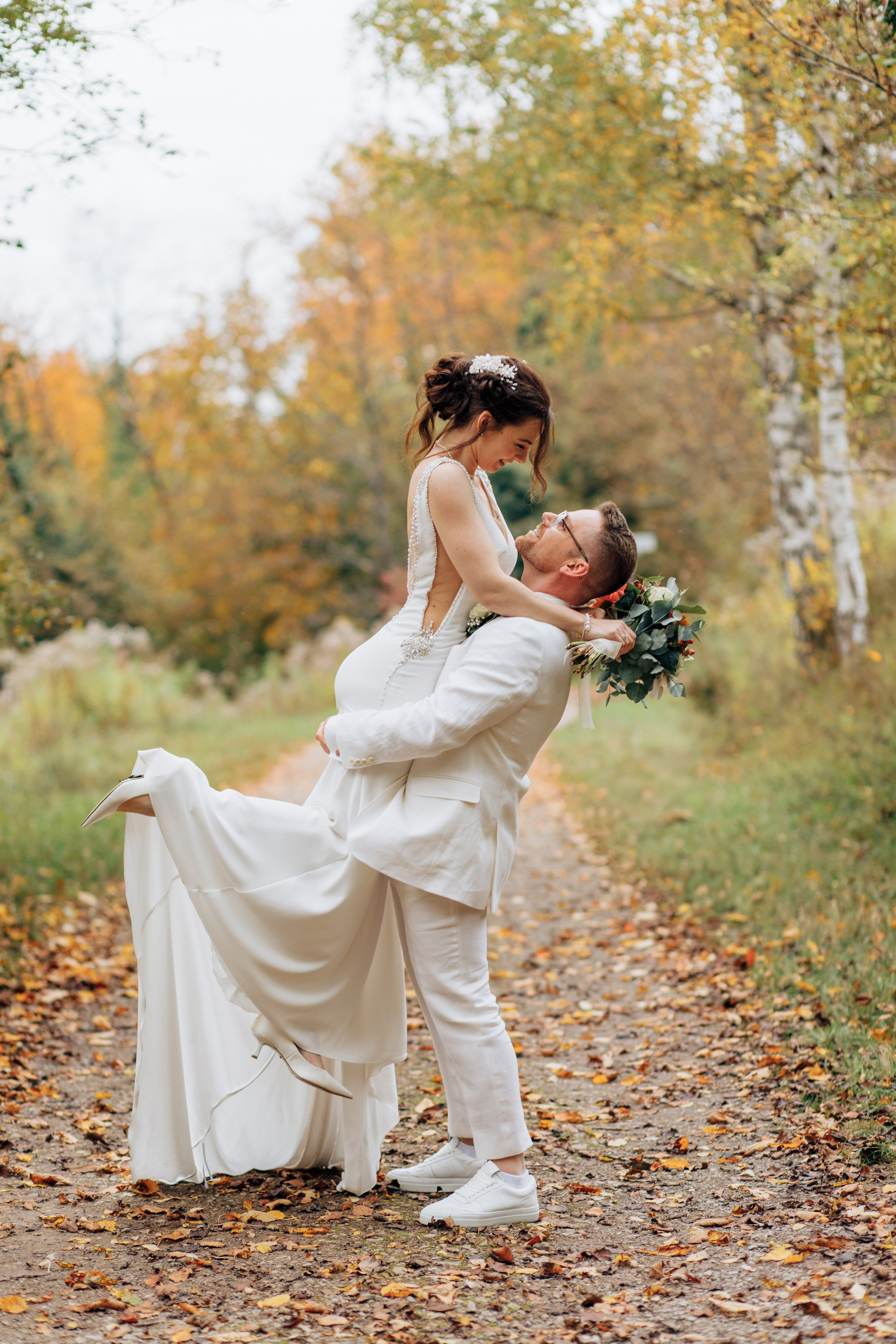 Der Bräutigam hebt die Braut elegant in die Luft, während sie ihn umarmt, und das alles im herbstlichen Wald.