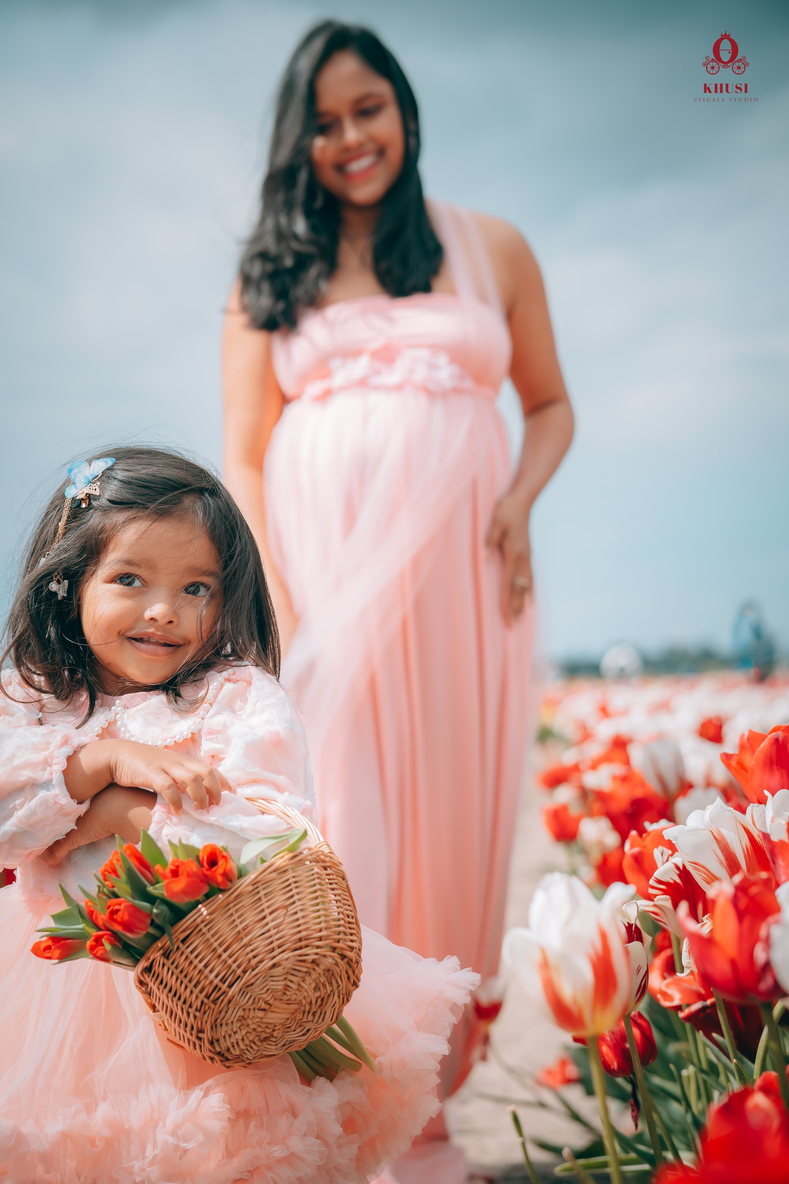 A girl holding a tulip flower basket and her pregnant mother looking at her in a tulip field in Netherlands
