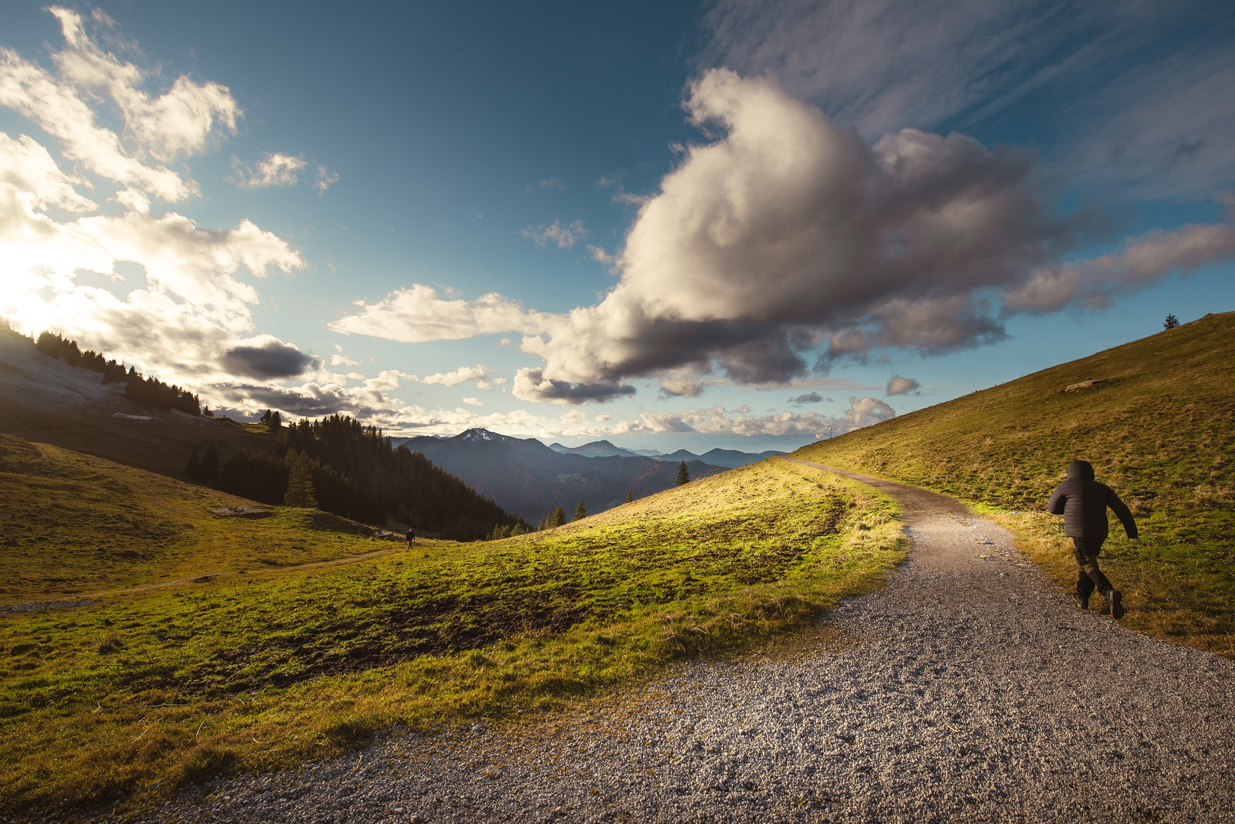 A lone runner on a gravel trail leading towards the Wallberg mountain summit․