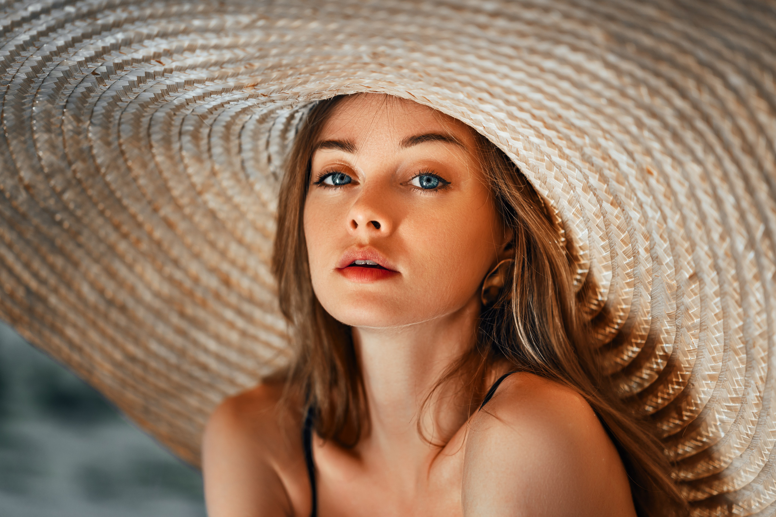 The close up portrait of model, in large hat, stands on the sandy shore, basking in the warm sunlight.