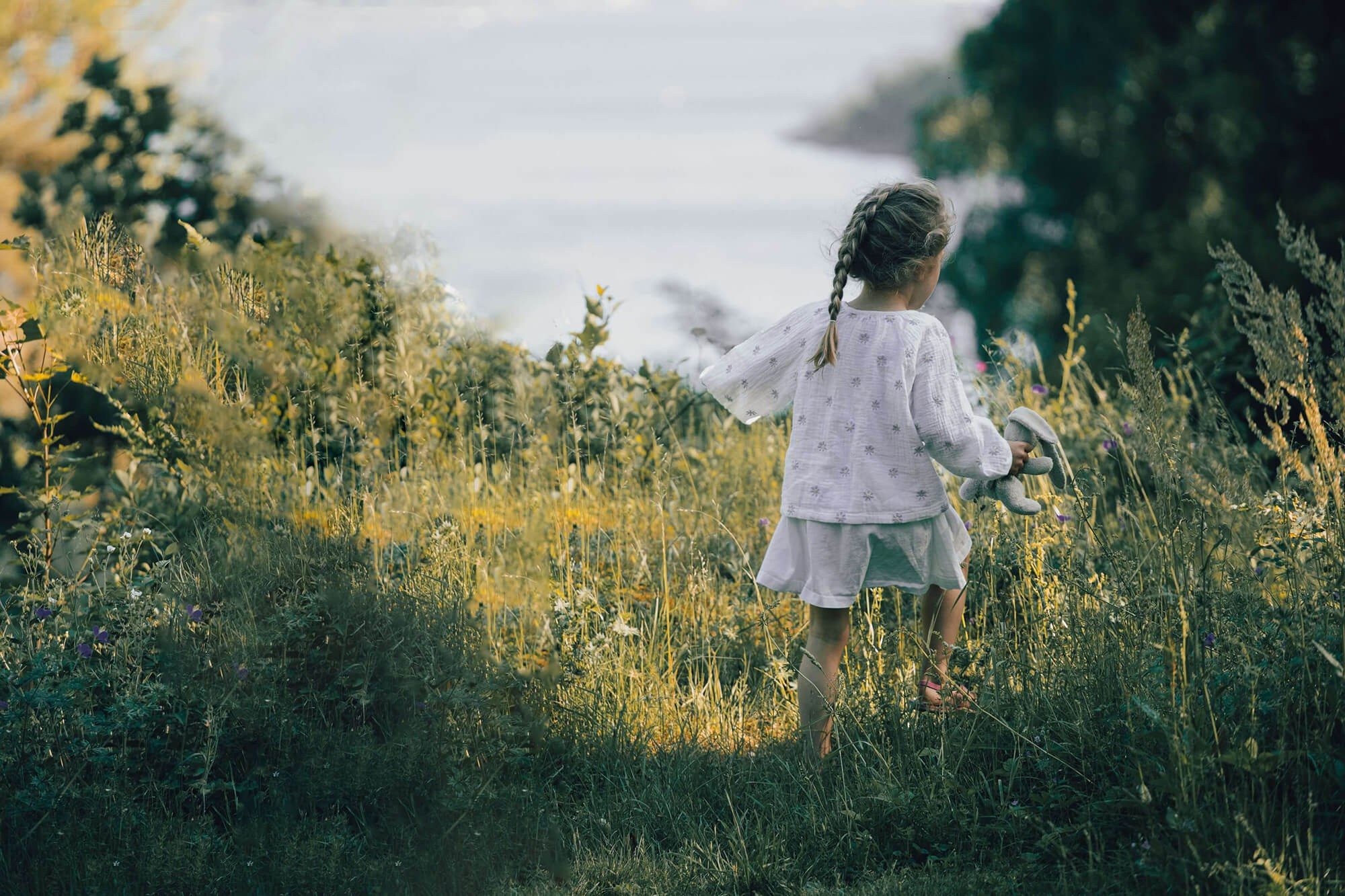 Barn løper i greset på ule Mor som holder babyen tett mens hunarde i POsgrunn