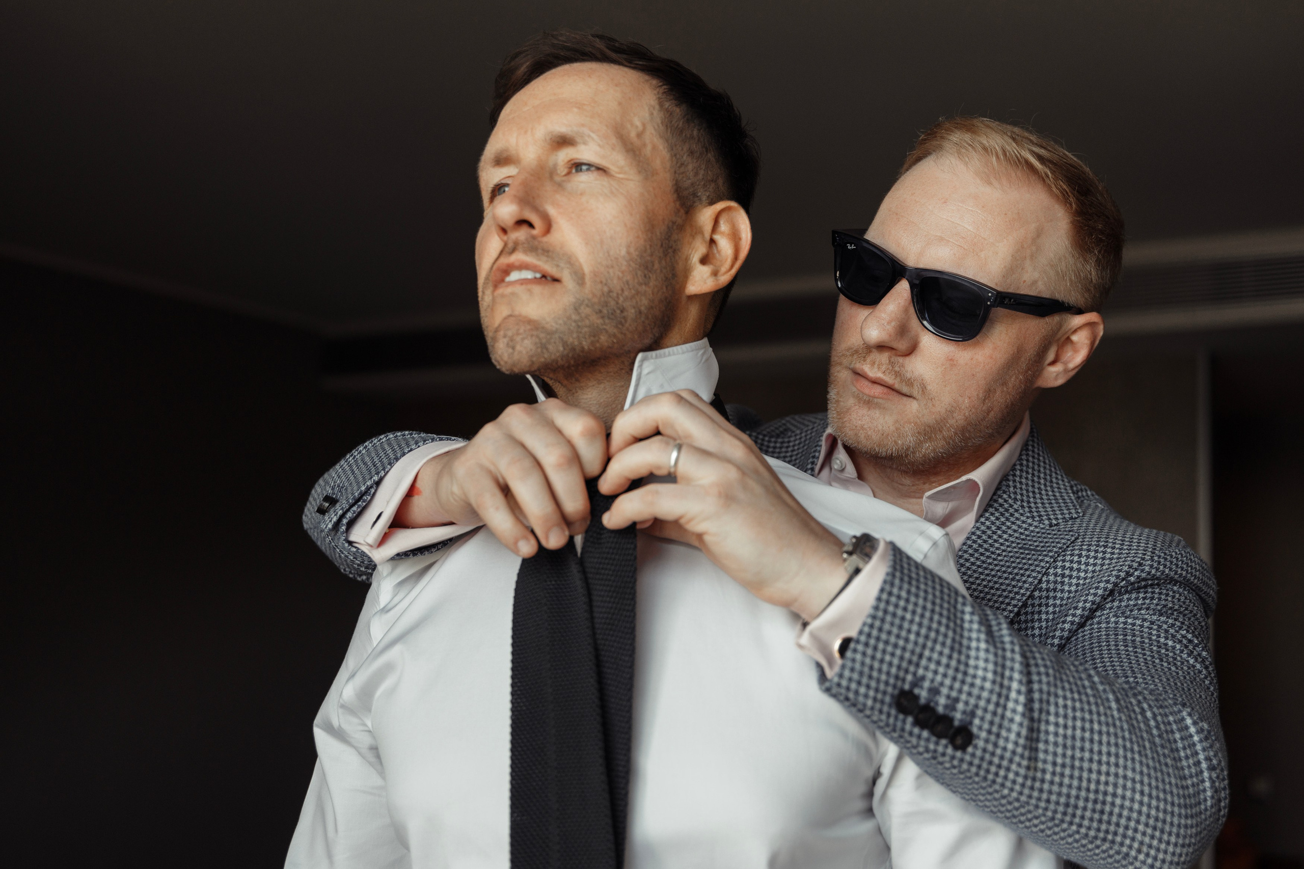 The groom getting ready in a cozy room, with his best man helping him put on his tie, on the big day at the hotel in Rhodes, Greece