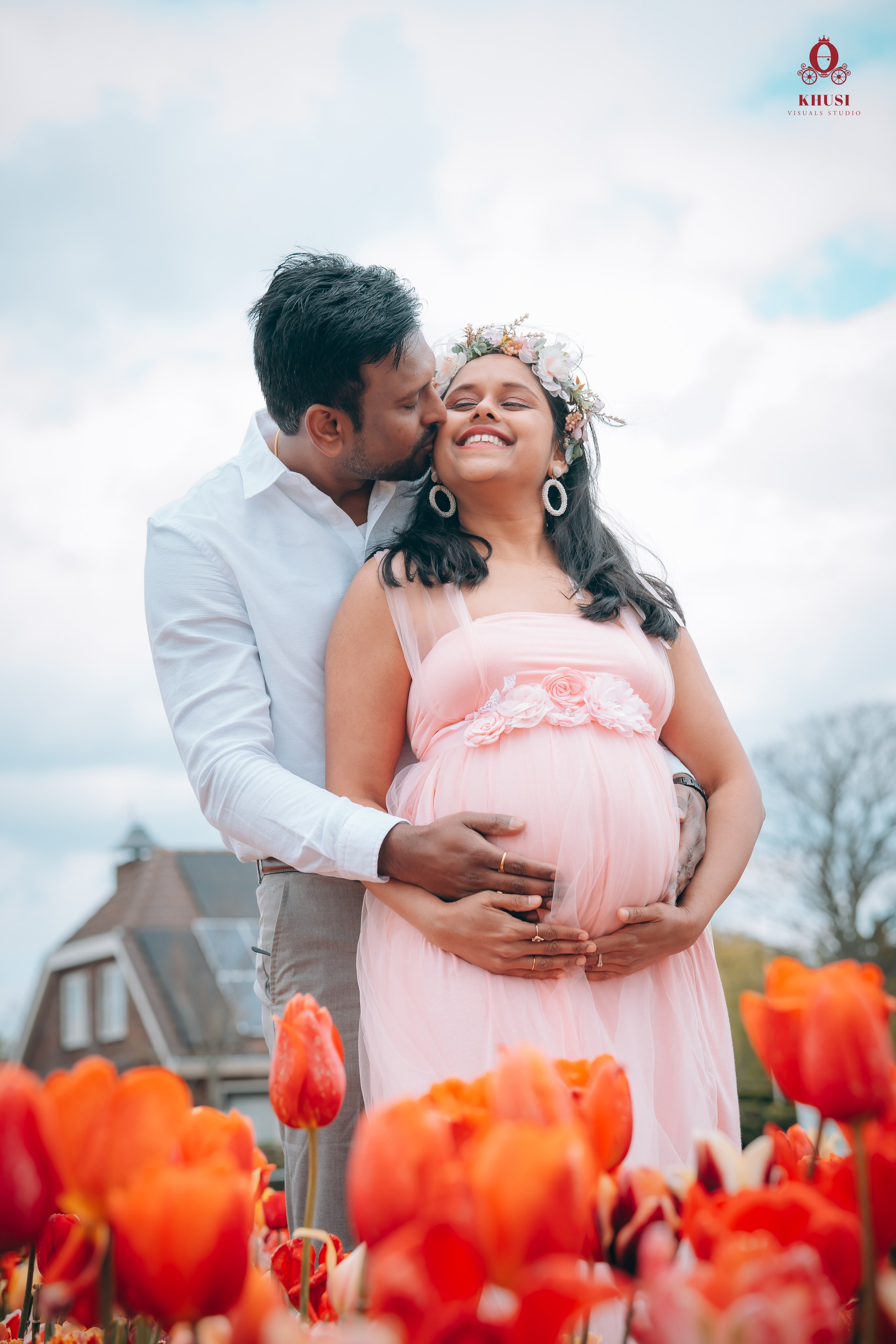 A husband kissing her pregnant wife on her cheeks and  in a tulip flower fields in Netherlands
