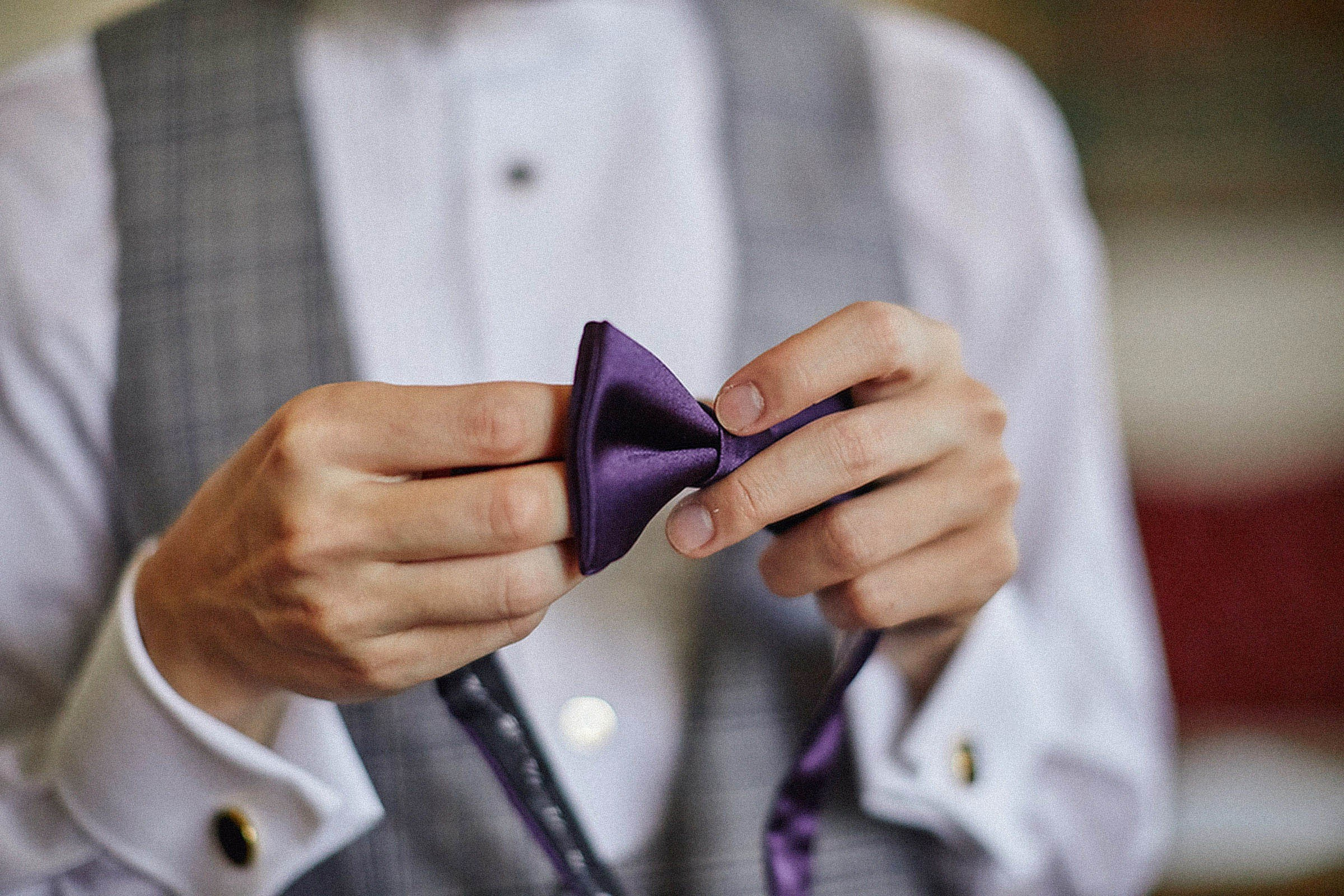 Groom's hands tying vivid purple bow tie detail Vila Bled.