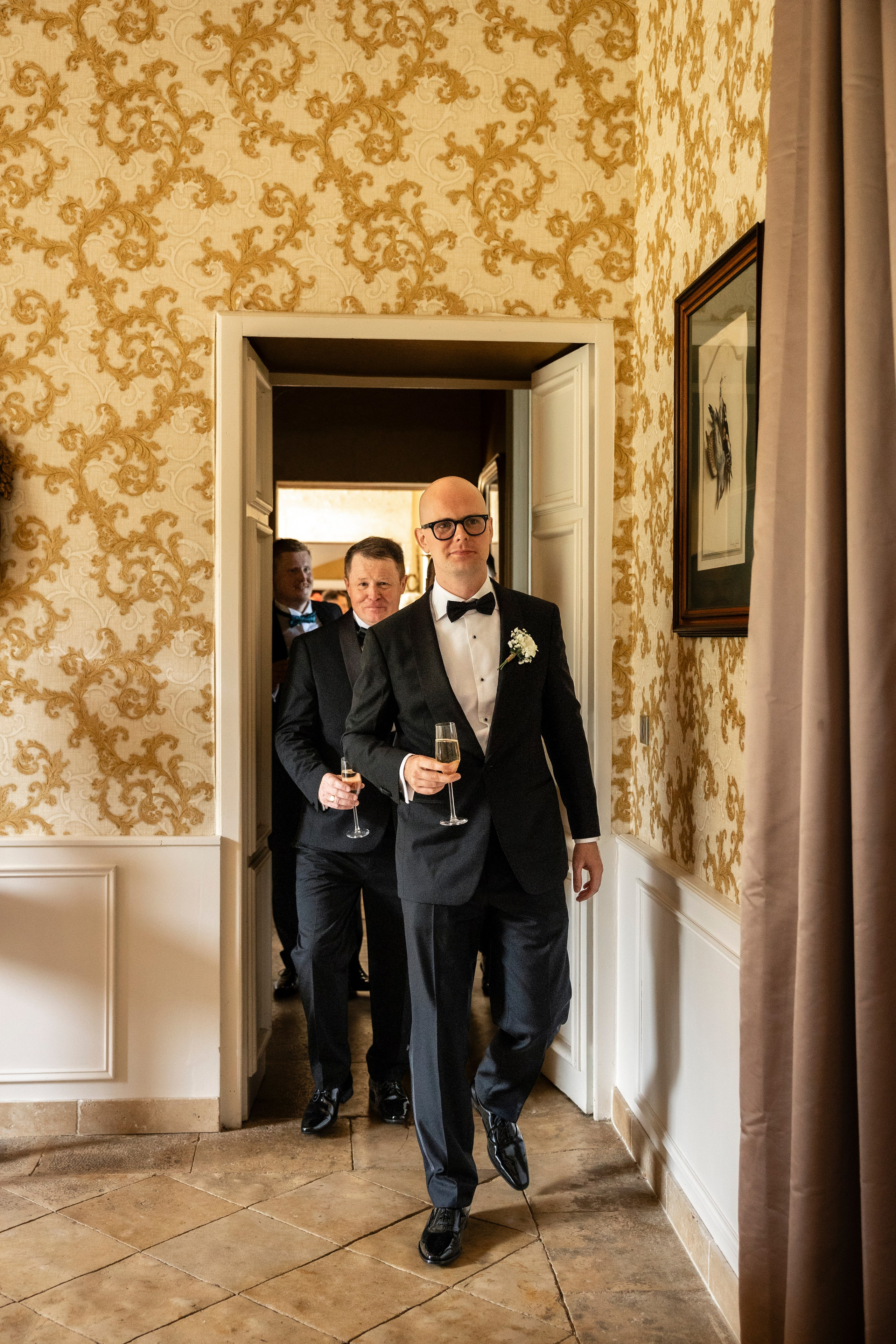 Groom walking through a doorway with yellow damask wallpaper