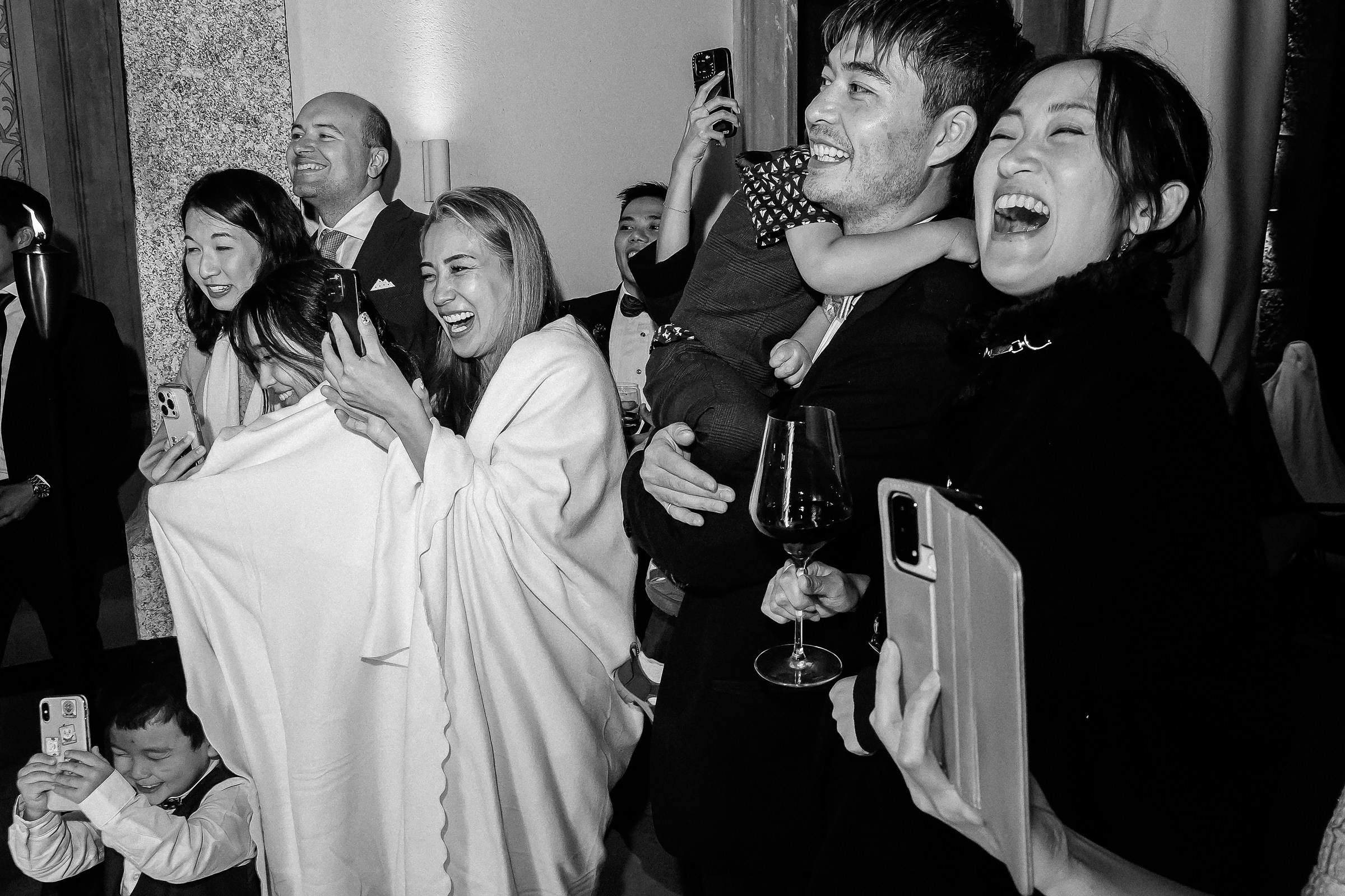 Guests cheer and laugh, capturing a joyful moment with phones during the wedding celebration.