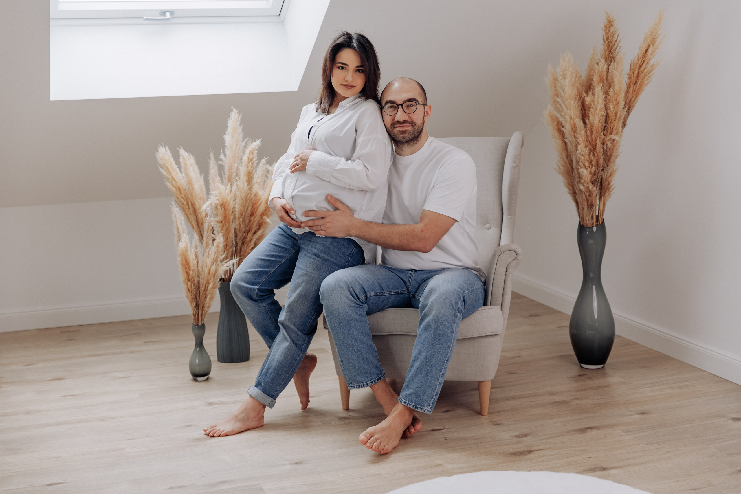 Schwangere Frau sitzt mit ihrem Mann auf einem Sessel im Fotostudio während eines Schwangerschaftsshootings.