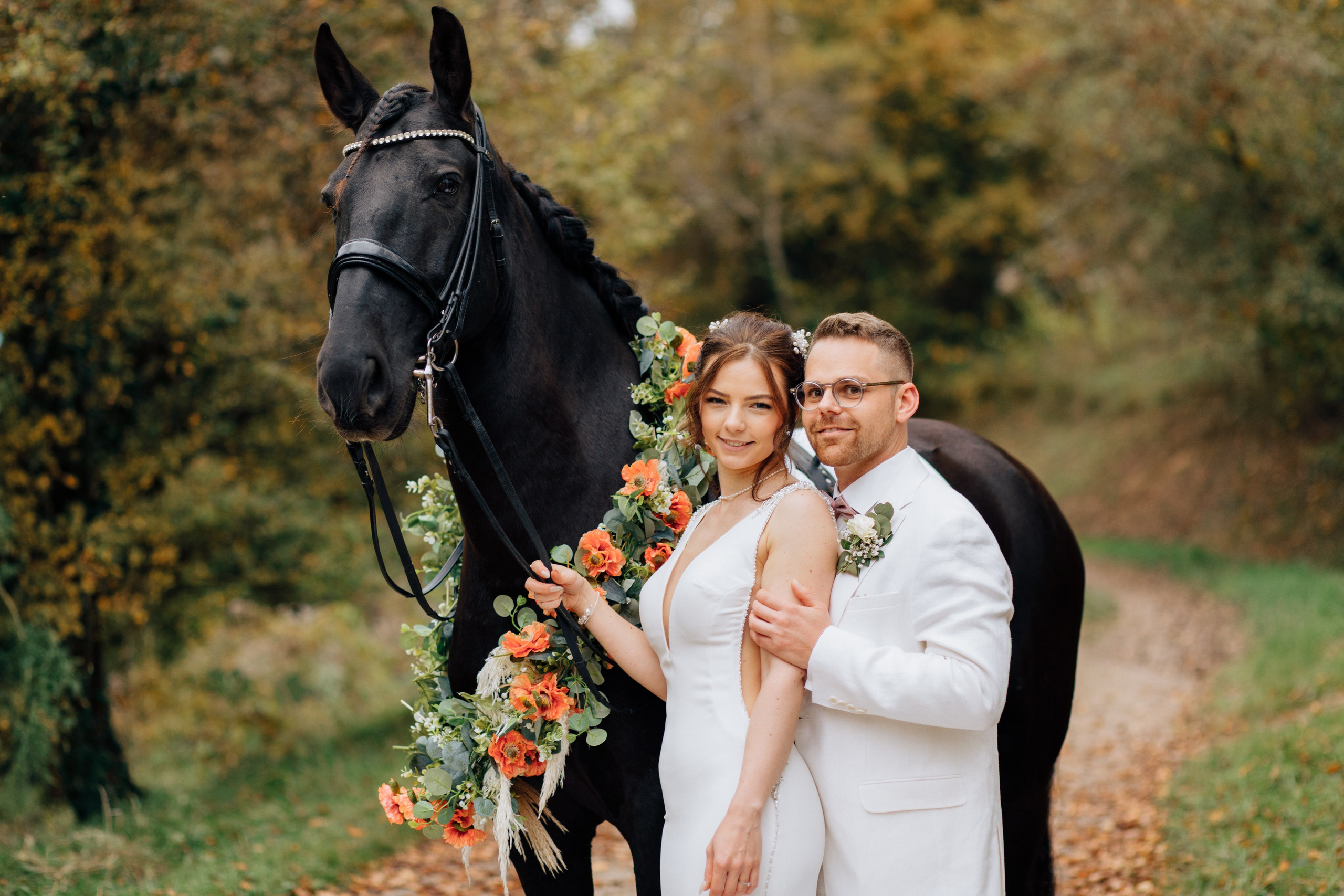 Der Bräutigam und die Braut lächeln, während das Pferd einen Blumenkranz trägt.