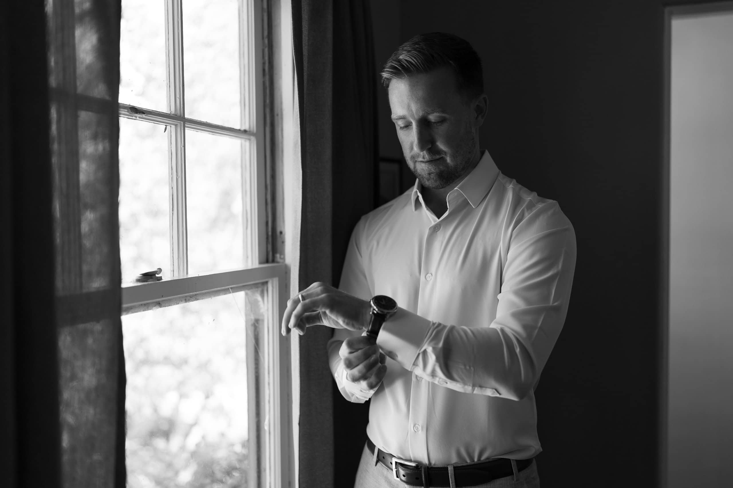 Groom adjusting cufflinks near window, pre-ceremony documentary moment 
