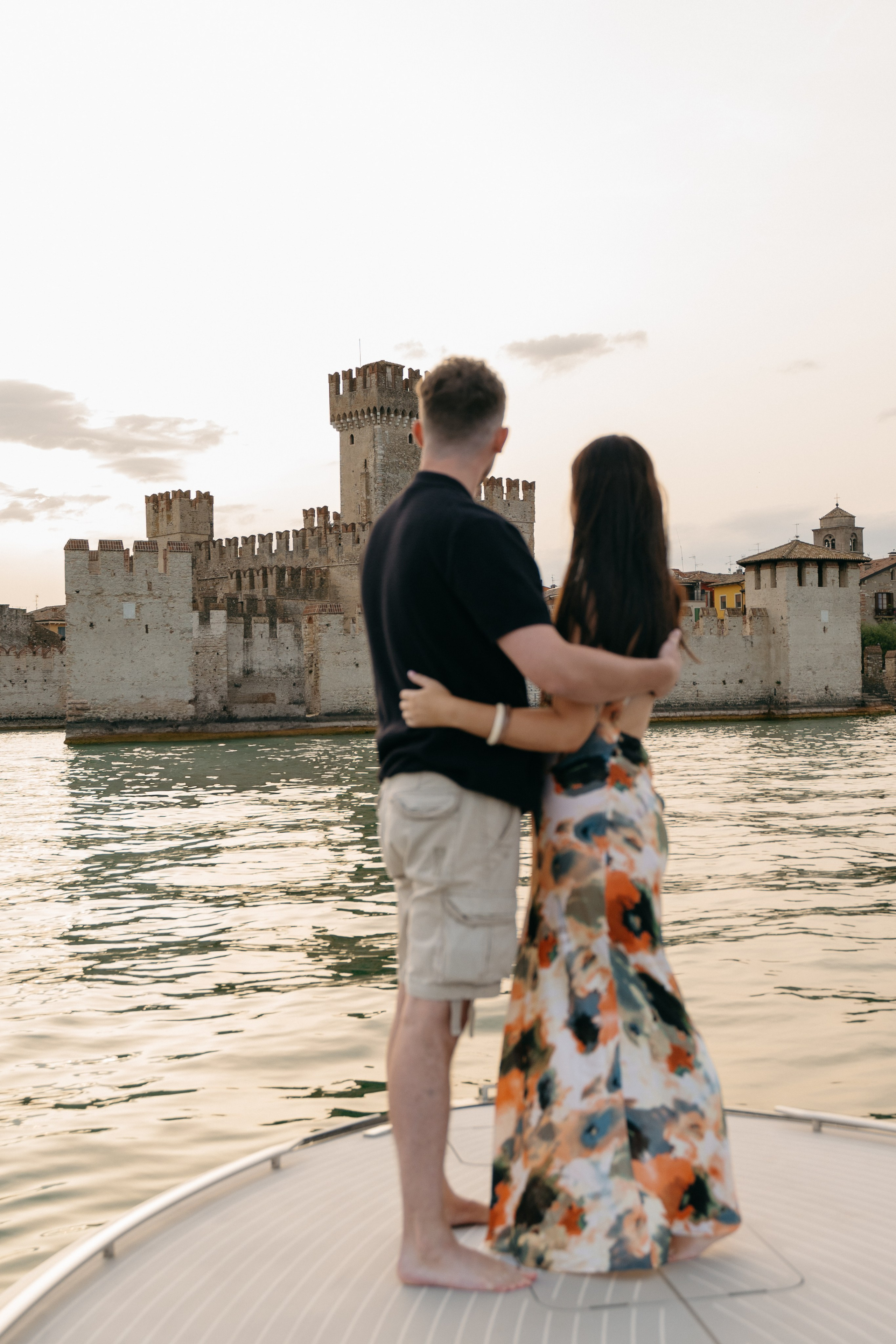 couple admiring the historic Sirmione skyline from their luxury boat at golden hour.