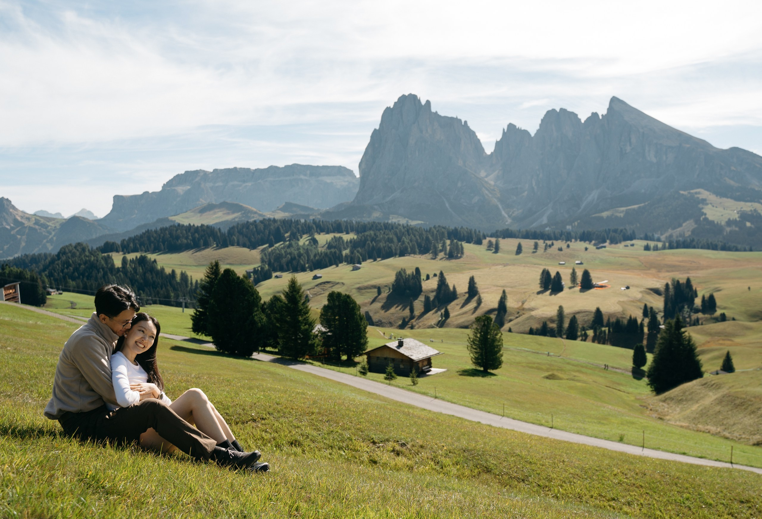 An Asian couple photographed from behind, facing the mountains after their Alpe di Siusi proposal.