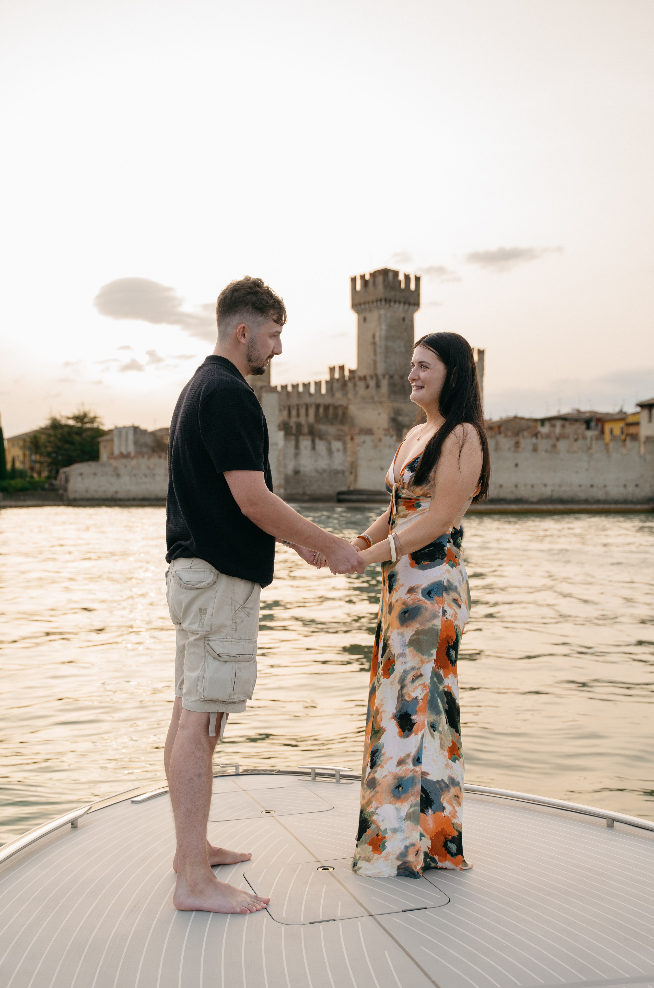 Elegant couple portrait aboard a private boat with the medieval walls of Sirmione behind them.
