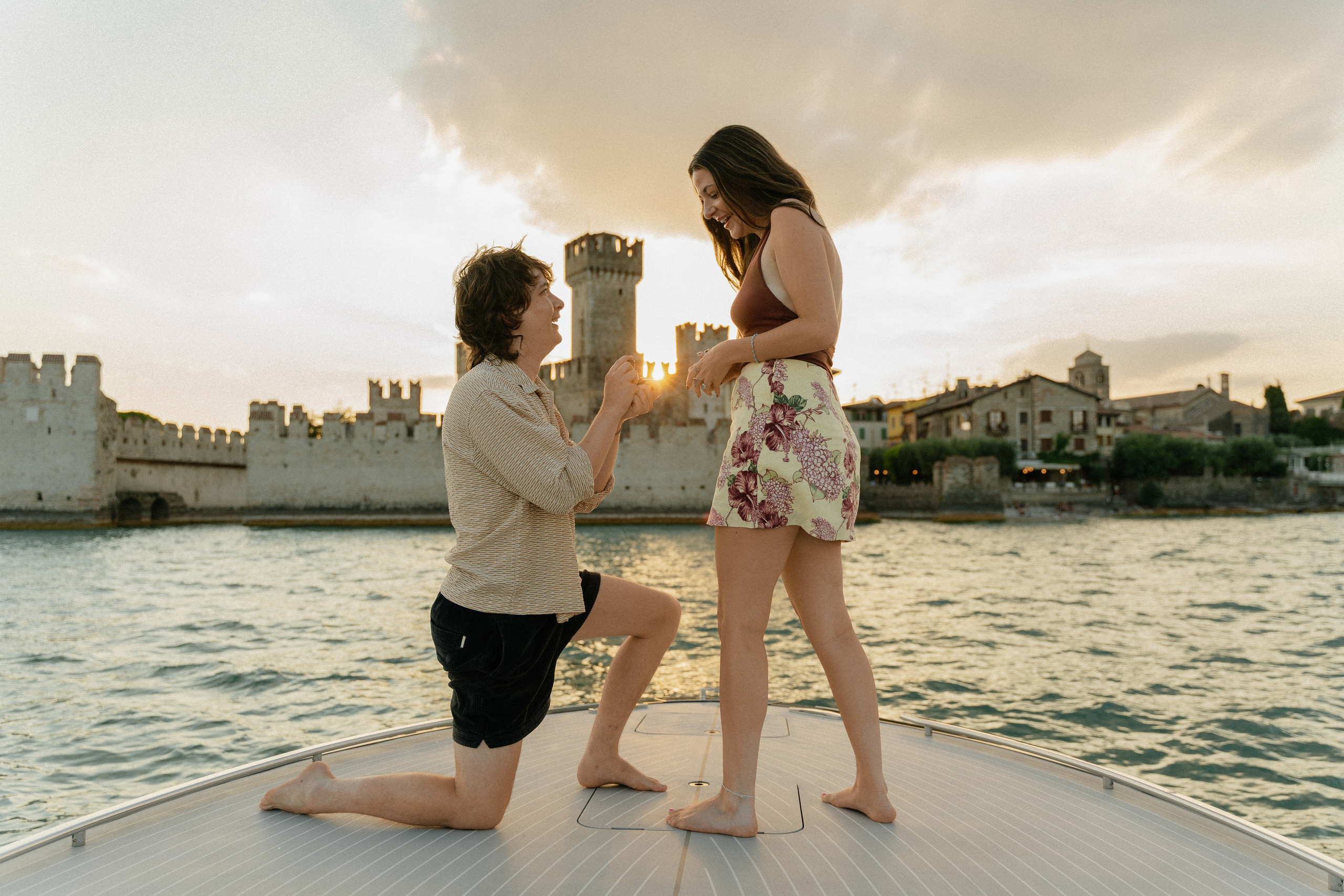 Emotional reaction after a surprise marriage proposal aboard a boat near Sirmione Castle.