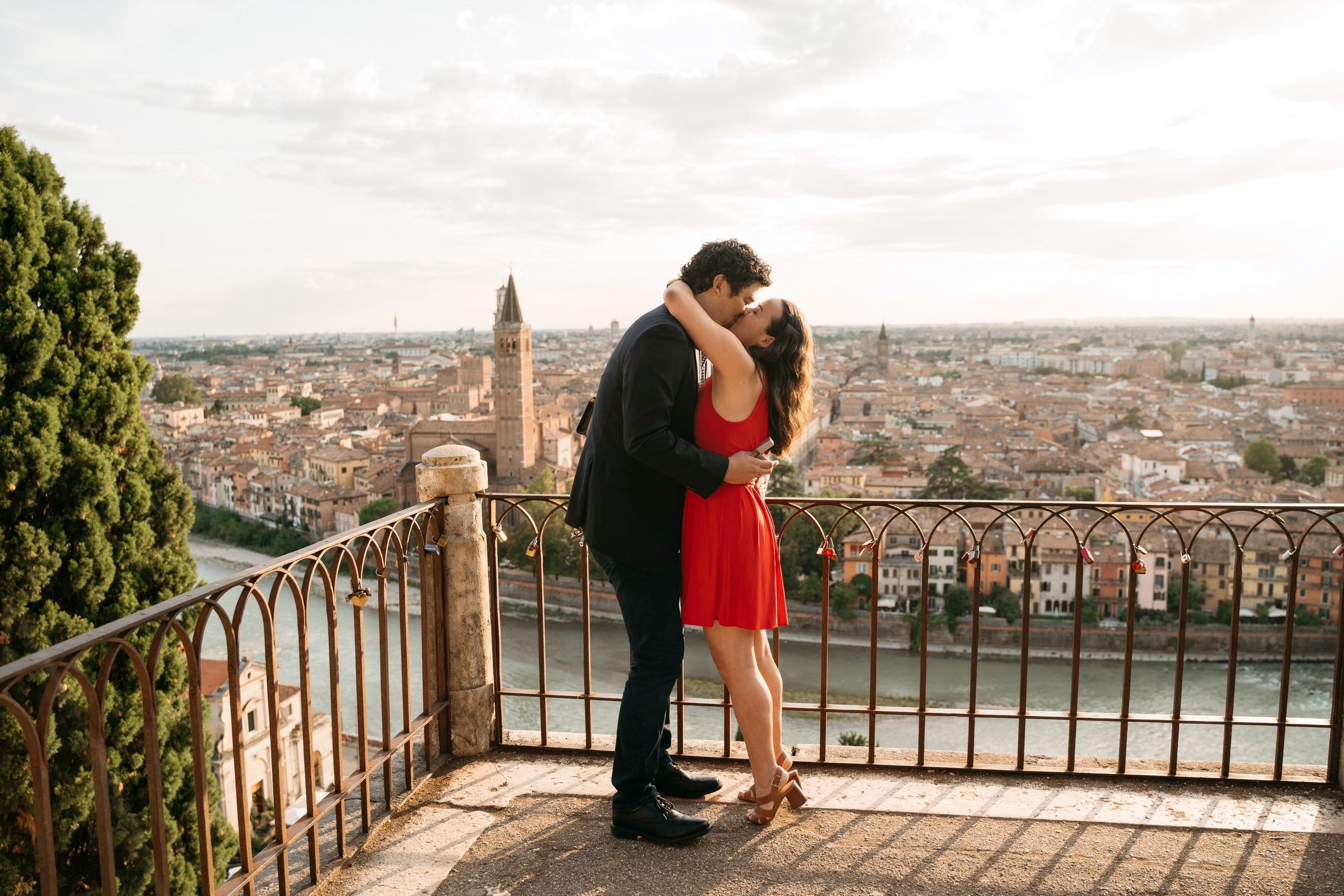 Newly engaged couple embracing above the rooftops of Verona at sunset.