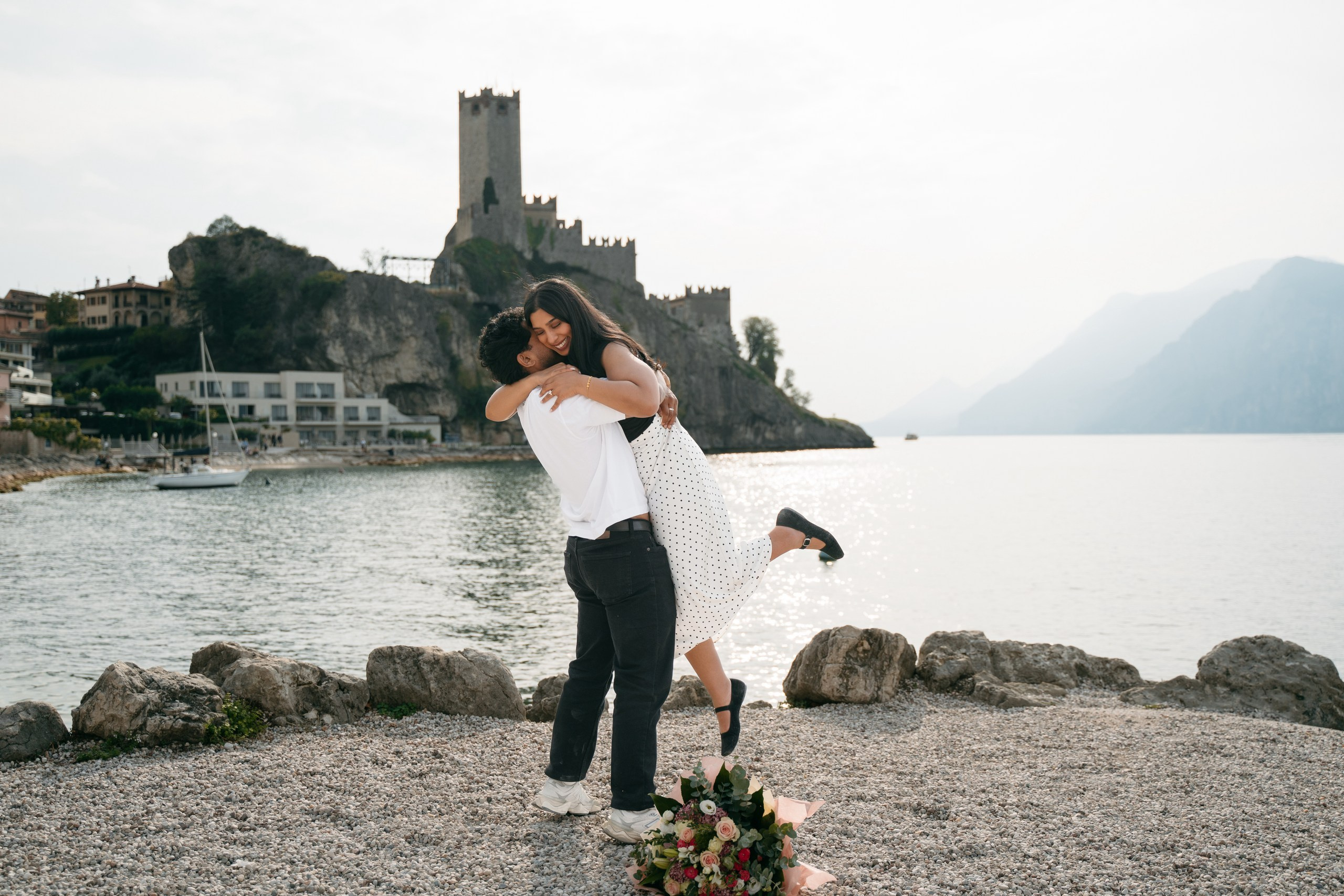 A couple embracing after their marriage proposal with views of Lake Garda.