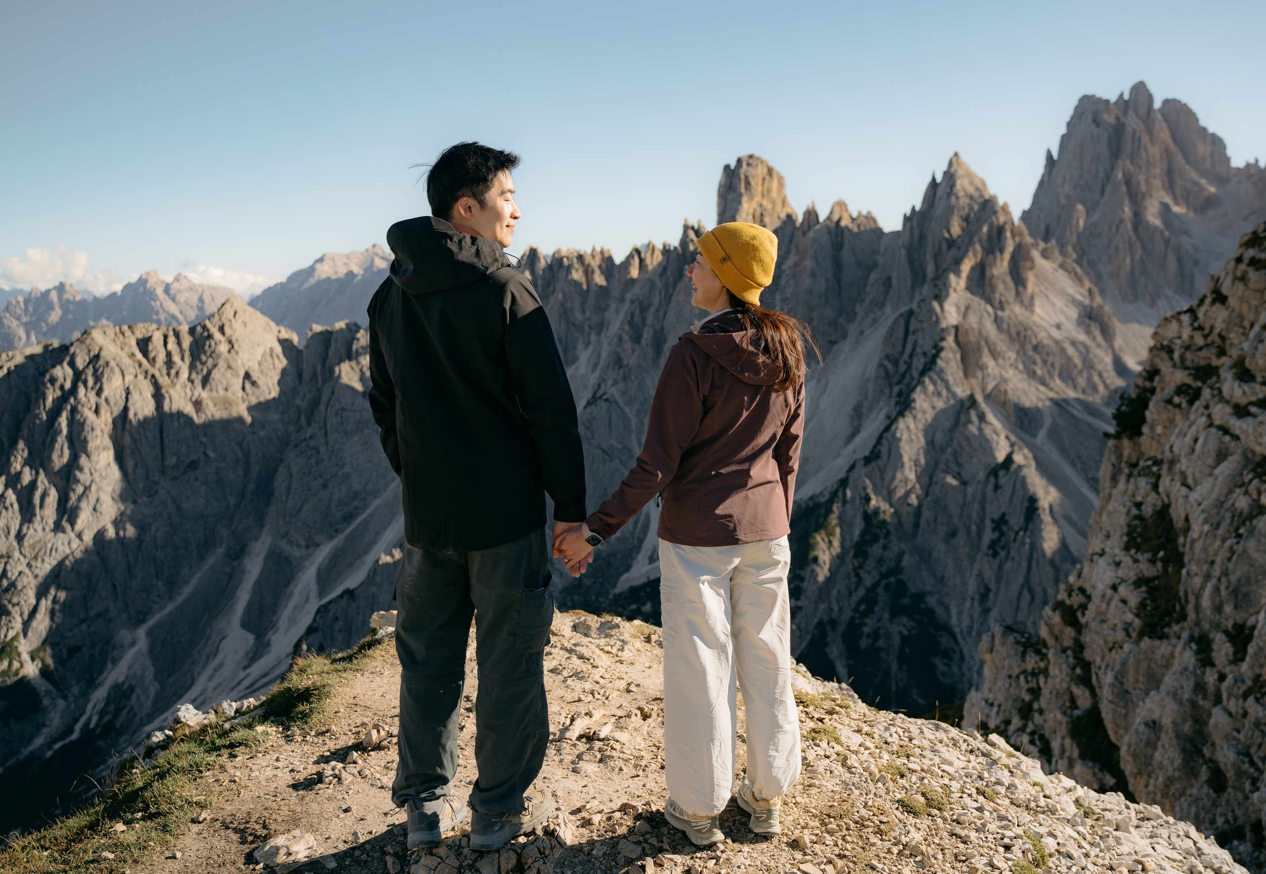 An Asian couple facing the Dolomite peaks, photographed from behind after their marriage proposal.