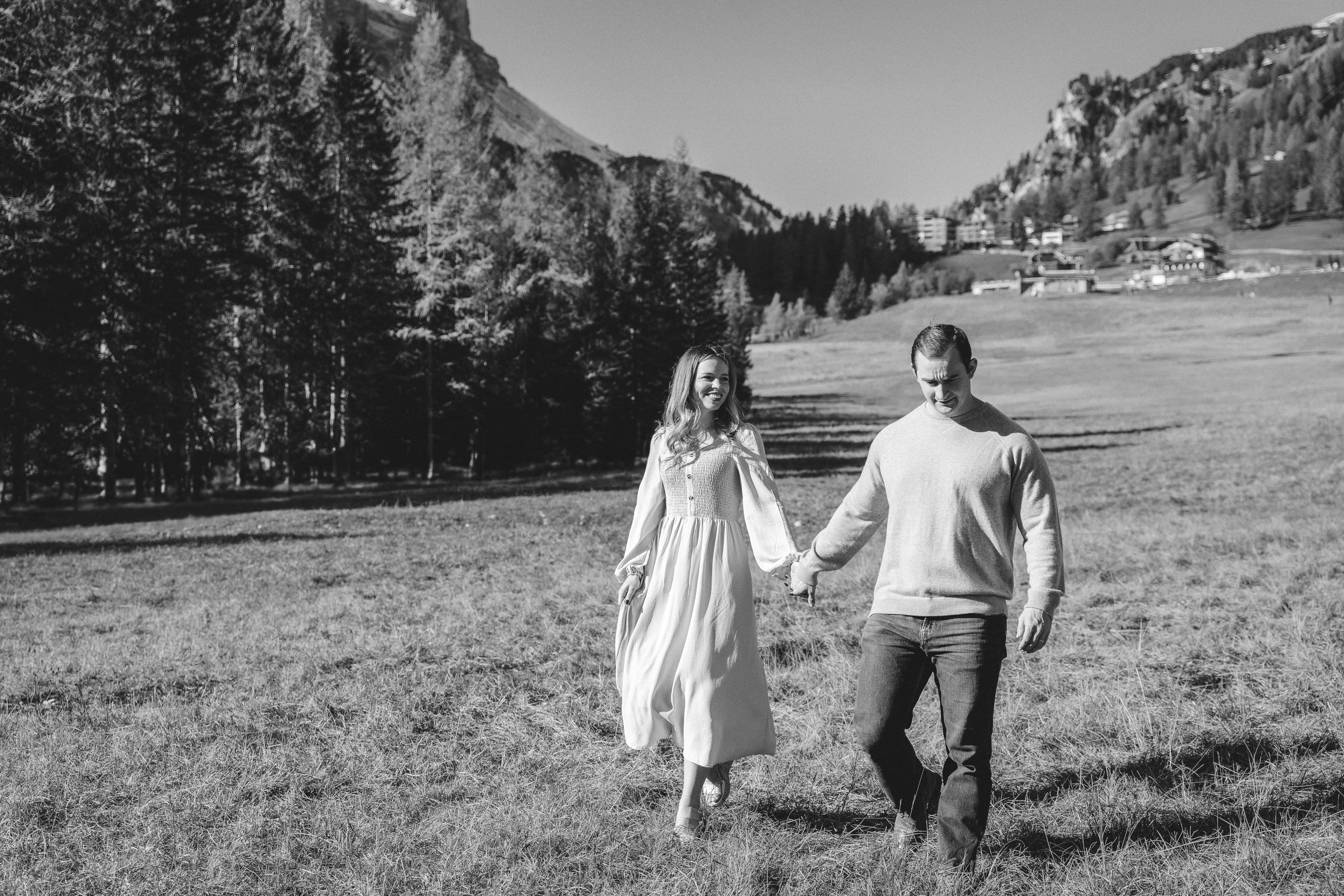 Couple holding hands with rugged Dolomite peaks rising behind them in Alta Badia.