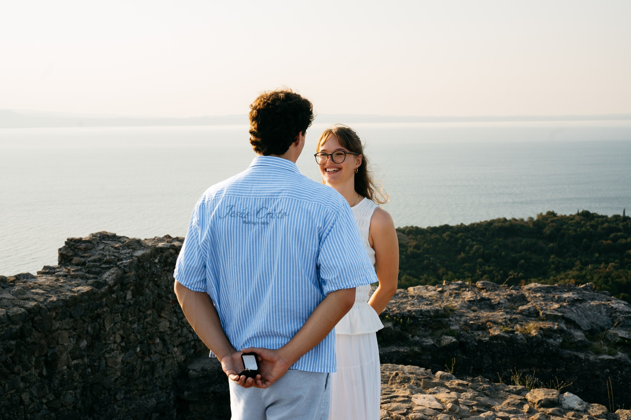 A young couple getting engaged at Rocca di Manerba with Lake Garda in the background, early in the morning.
