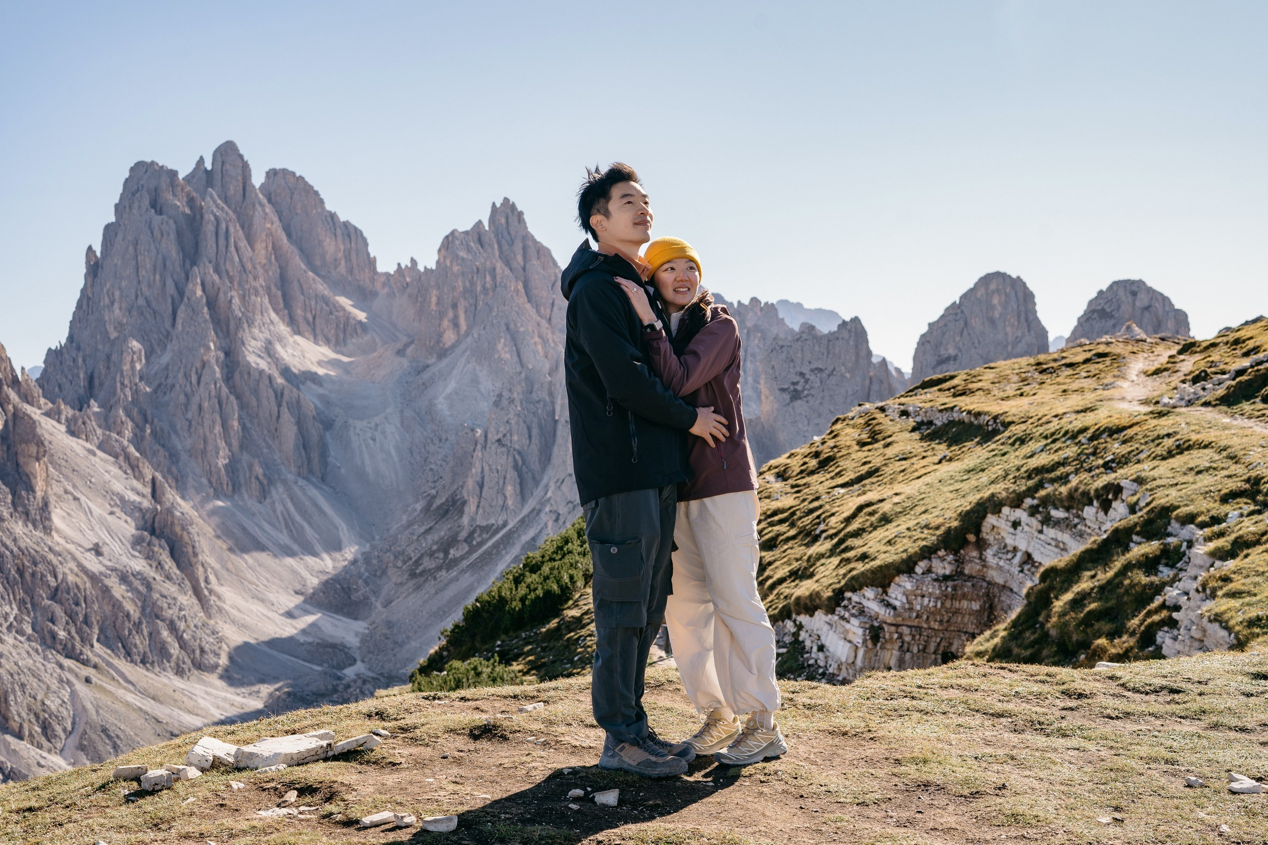 A wide view of an Asian couple’s proposal with the jagged peaks of Cadini di Misurina behind them.
