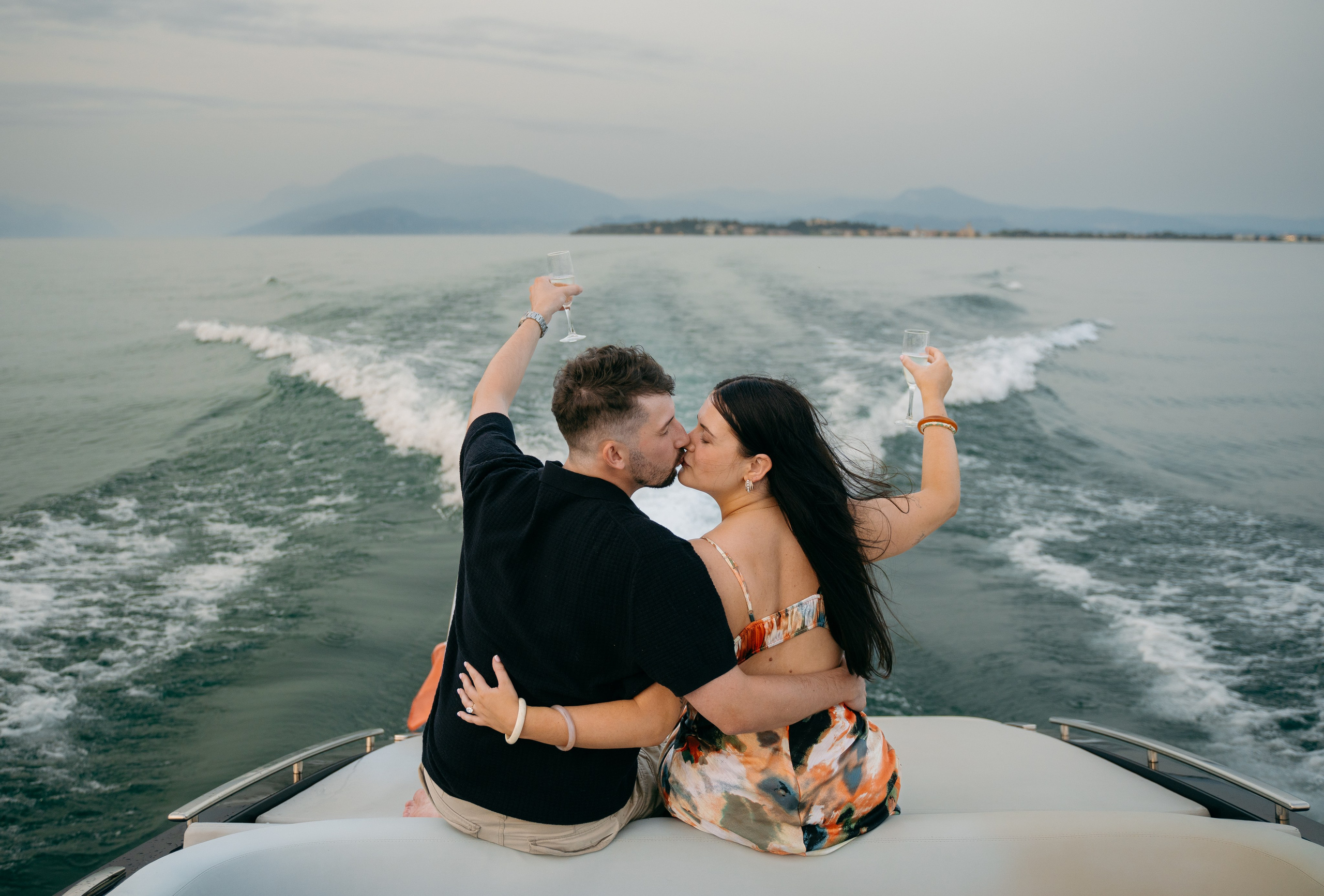 Newly engaged couple toasting with champagne aboard a luxury boat in Sirmione on Lake Garda.