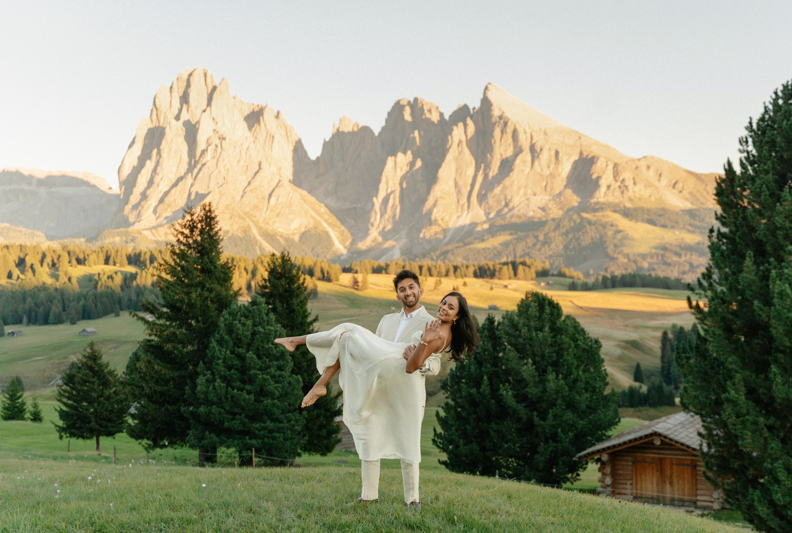 Newly engaged couple smiling together with Dolomites views behind them.