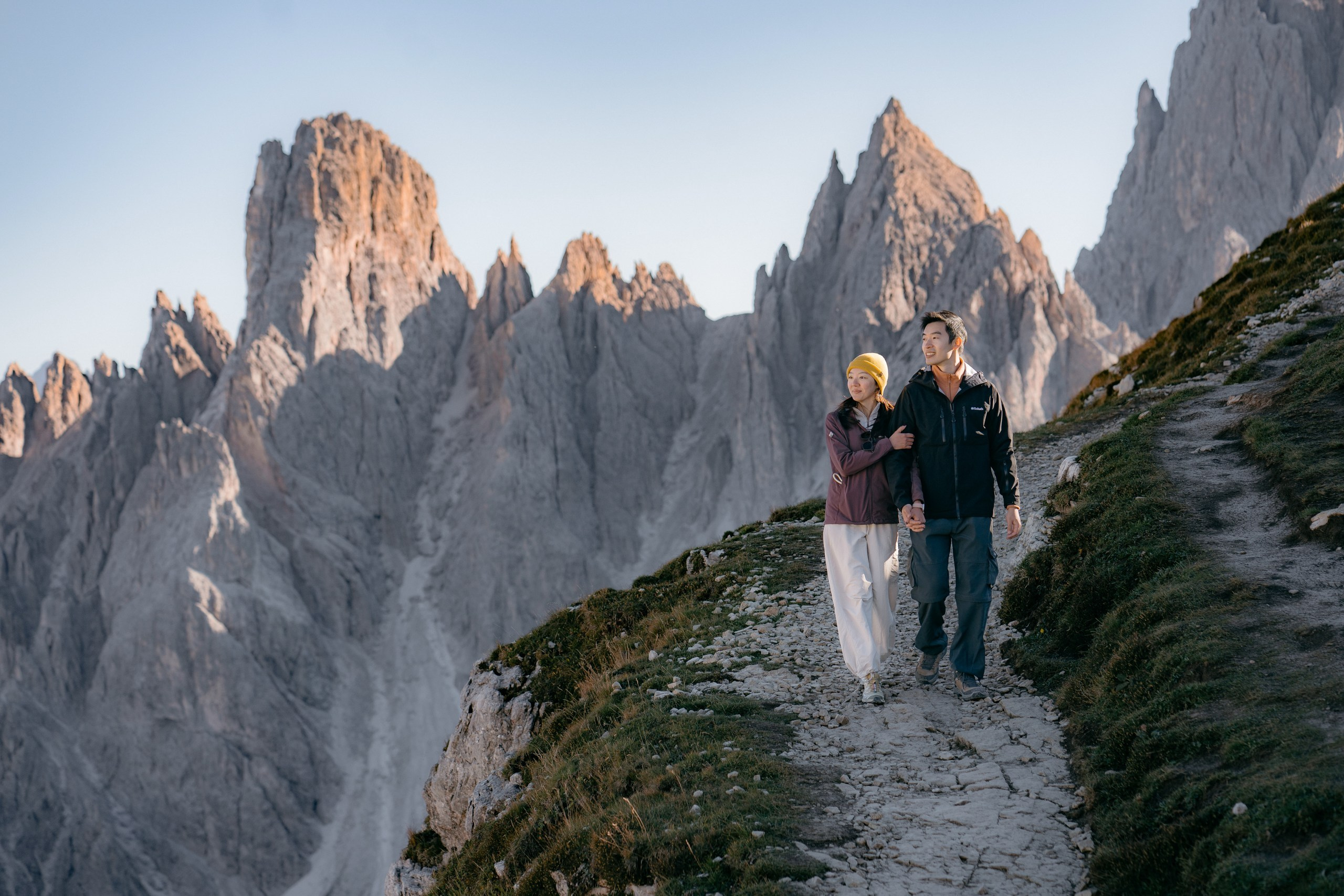 A distant view of a newly engaged Asian couple surrounded by the mountain landscape of the Dolomites.