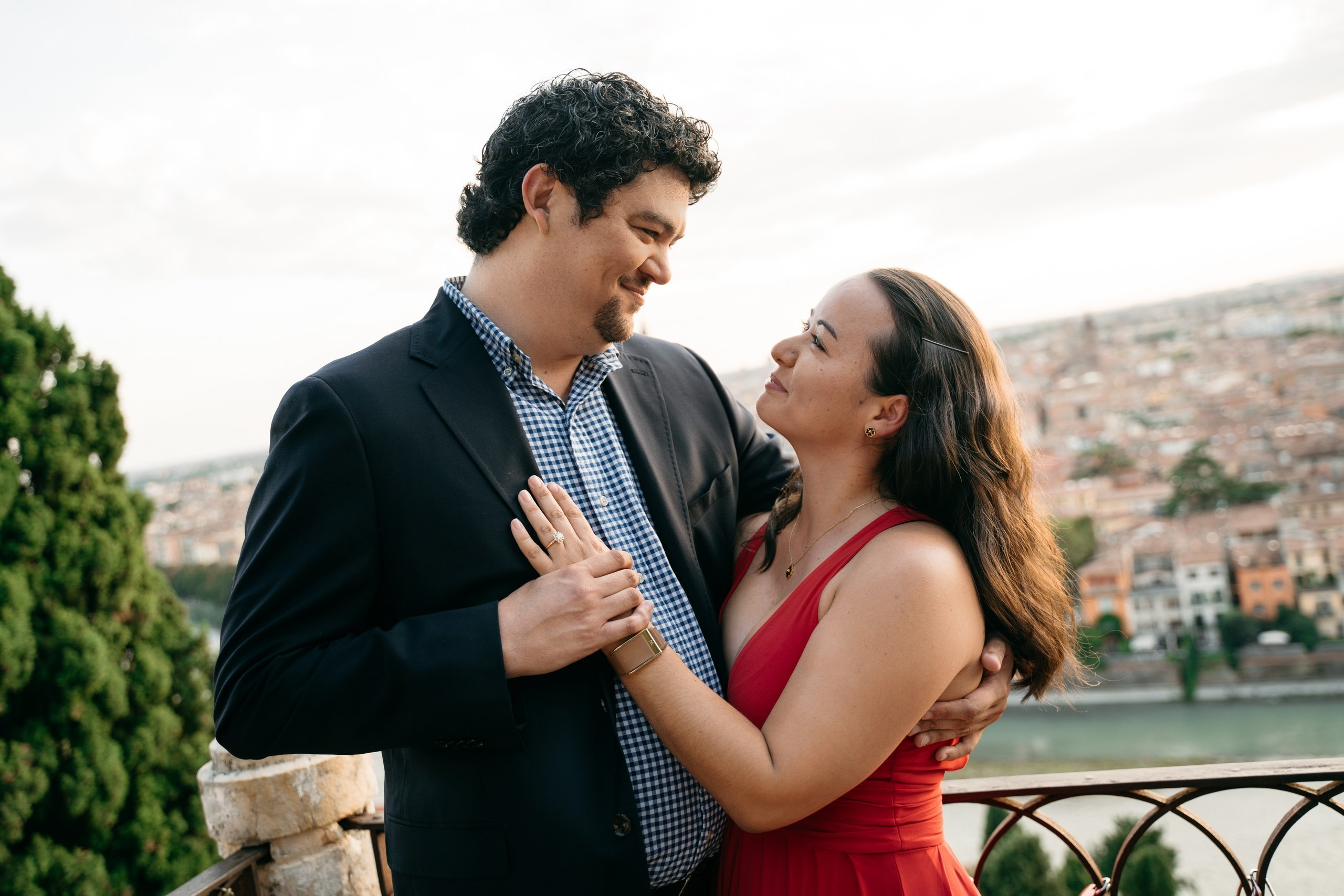 A couple smiling at each other moments after getting engaged overlooking Verona.