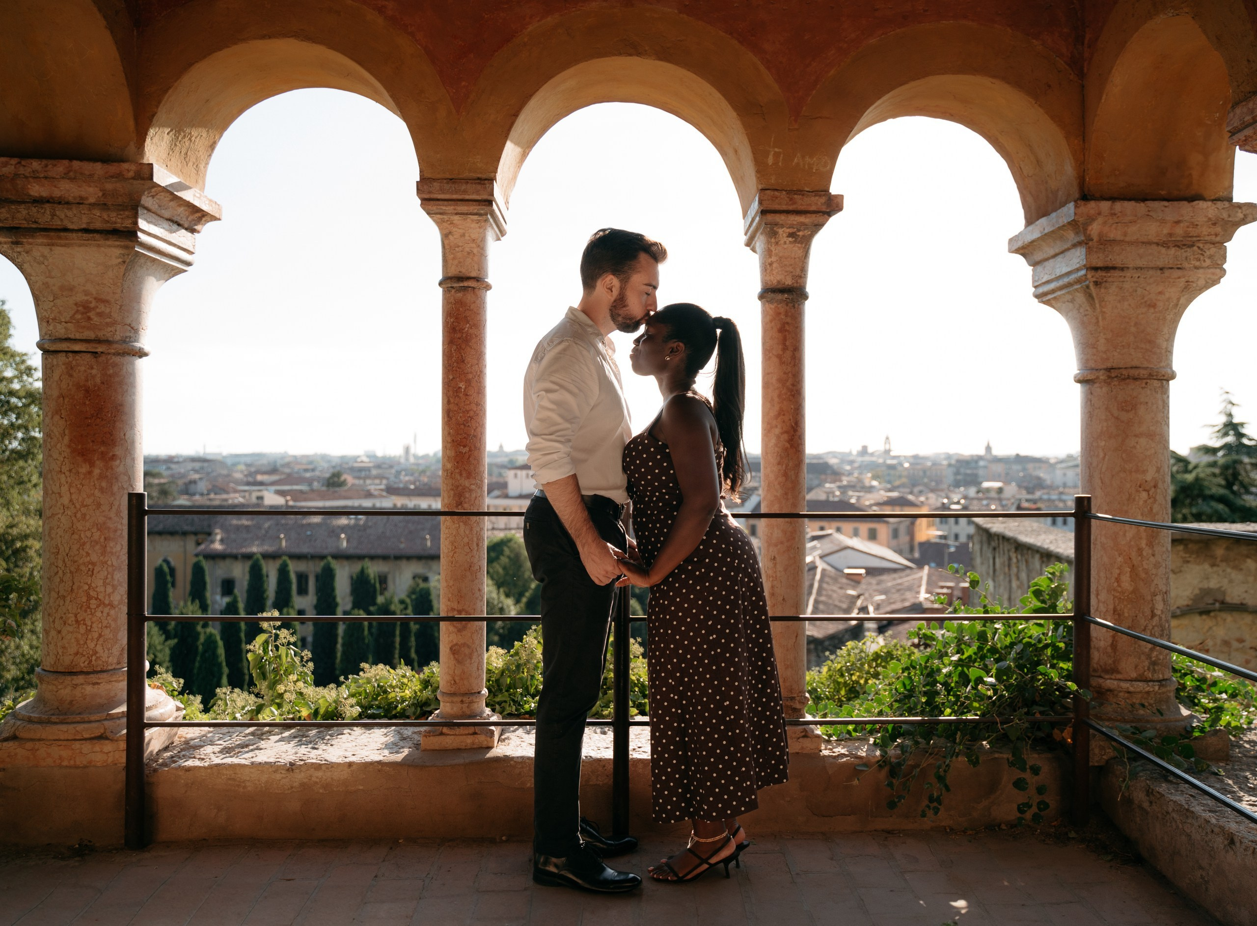 An interracial couple sharing a kiss after their proposal at Giardino Giusti, Verona.