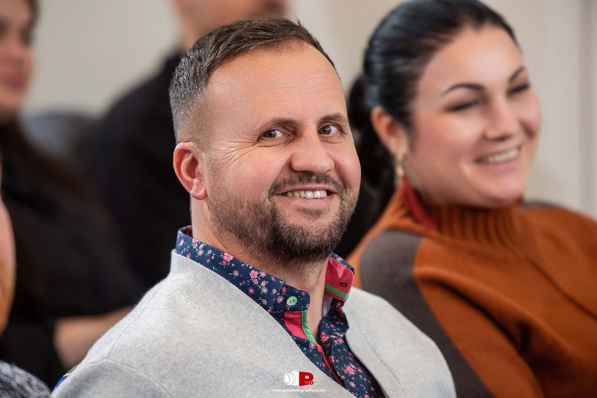 A smiling man attending a professional corporate event, dressed in a stylish floral shirt under a light grey blazer.