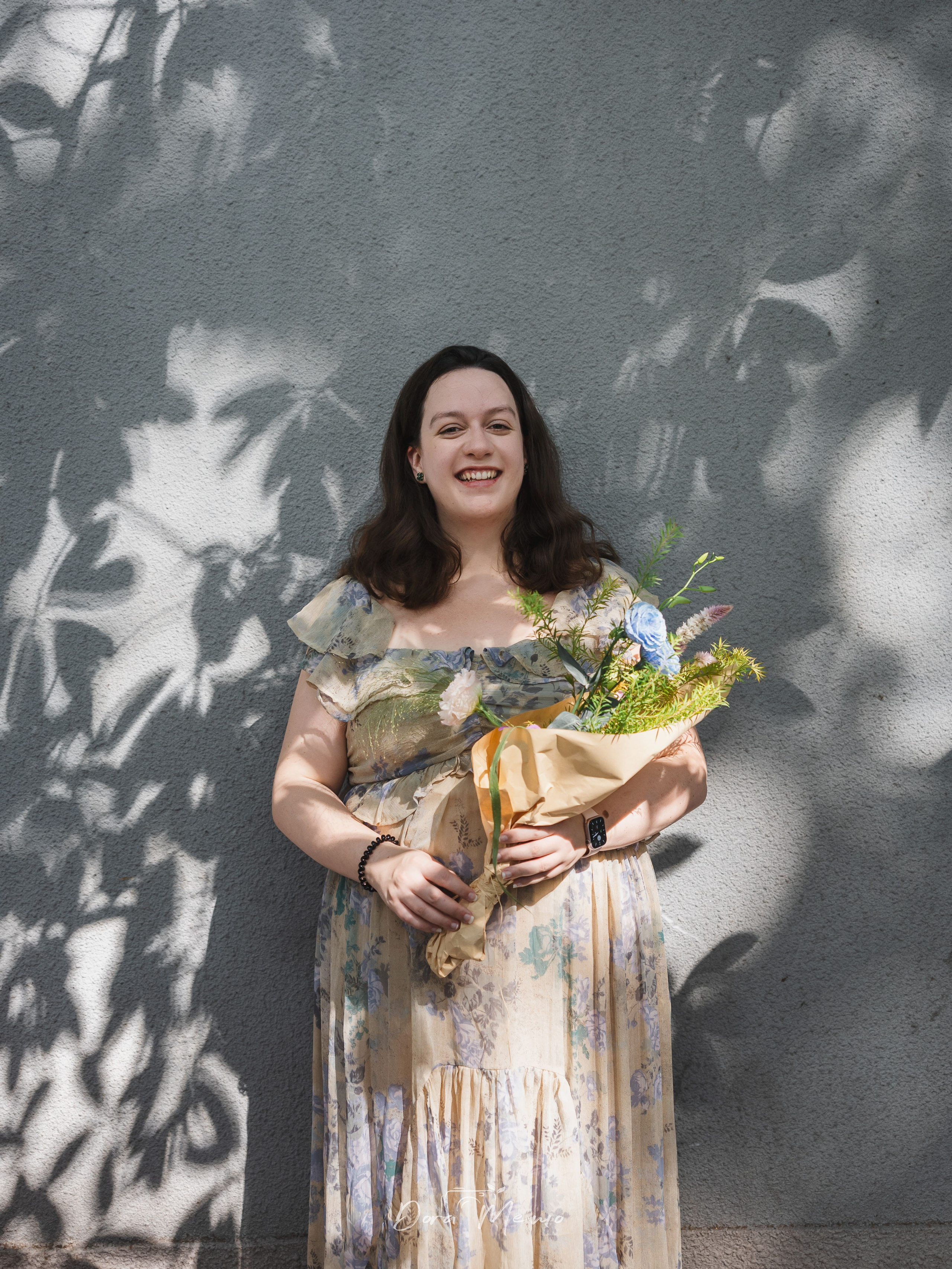 An expecting mother smiling with flowers against a wall covered in plane tree shadows in the Former French Concession.