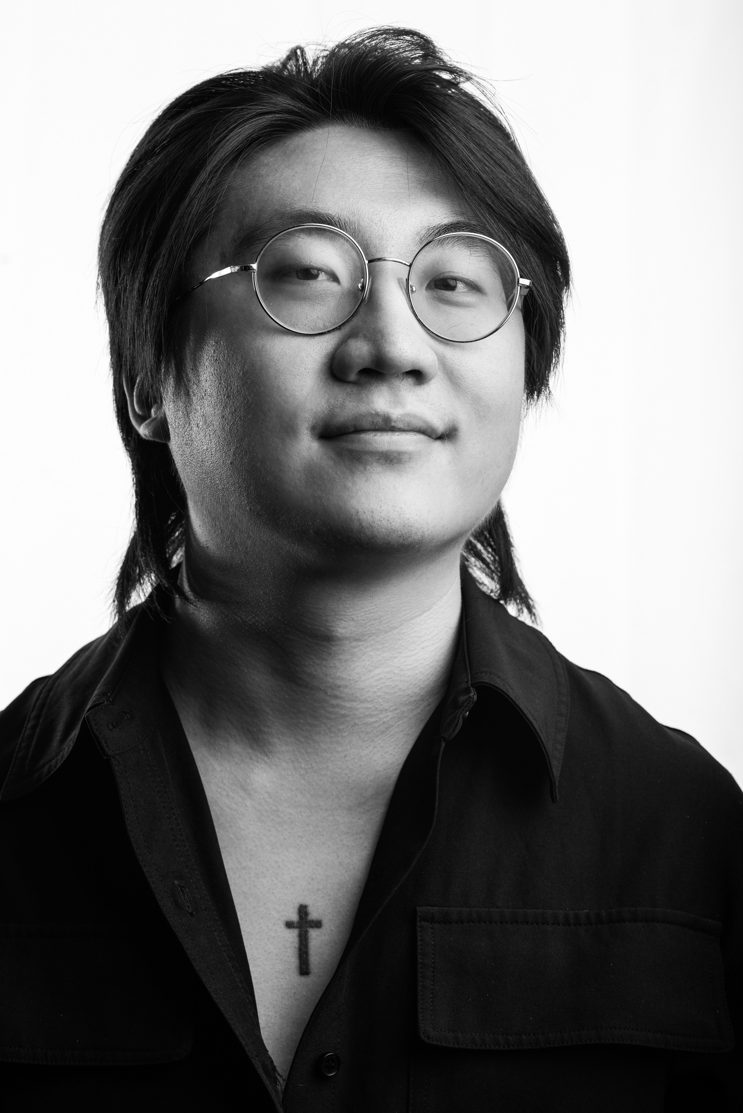 A striking black-and-white corporate portrait showcasing a young professional with medium-length hair and round glasses, wearing a dark button-up shirt. Captured against a clean white background, the image emphasizes the subject's confidence and modern style through soft lighting and precise composition. Perfect for demonstrating professional portrait photography for Singaporean businesses seeking polished, high-quality visuals.