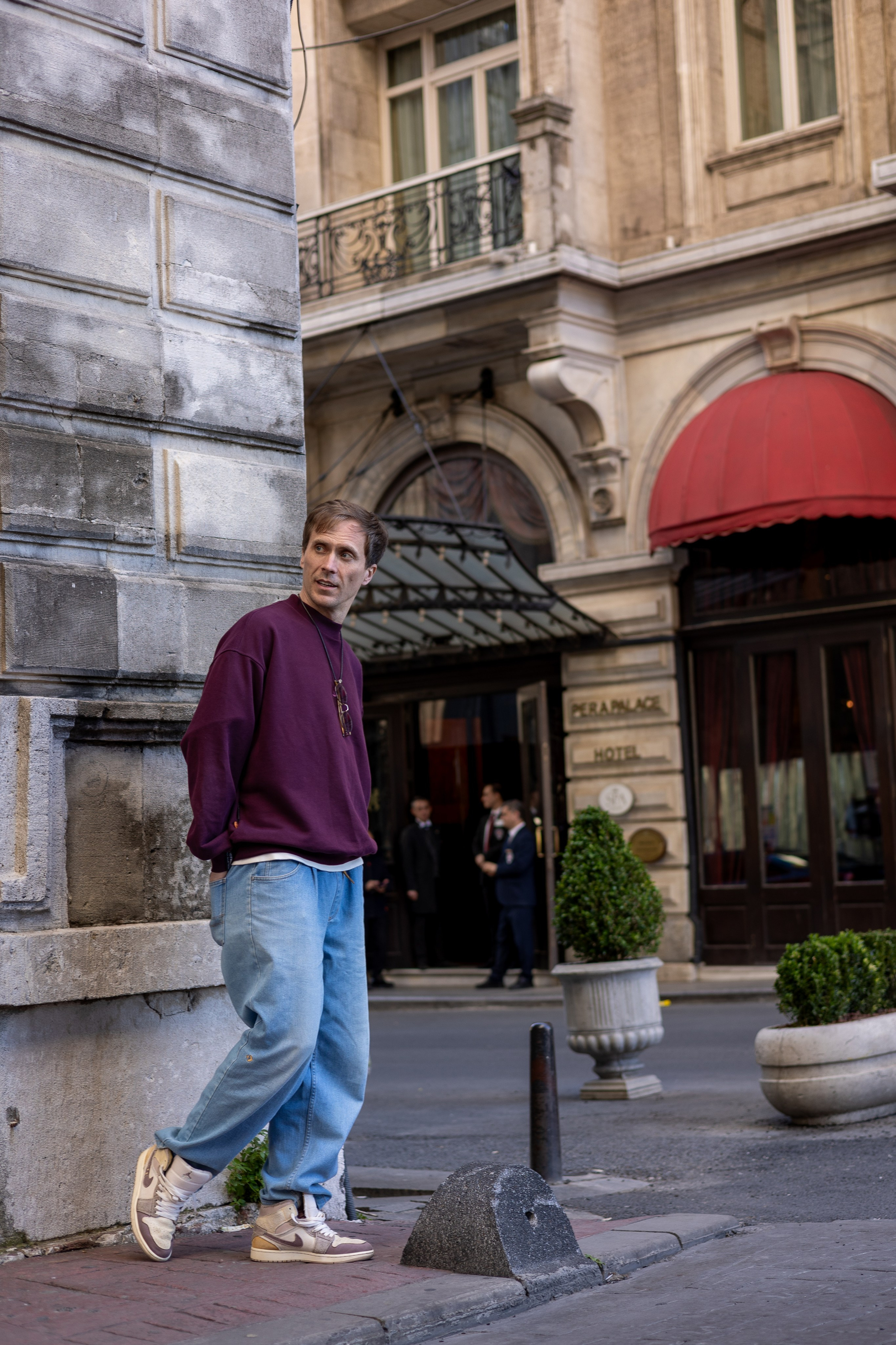 Мужчина стоит у угла каменного здания на городской улице рядом с отелем Pera Palace Hotel в Стамбуле